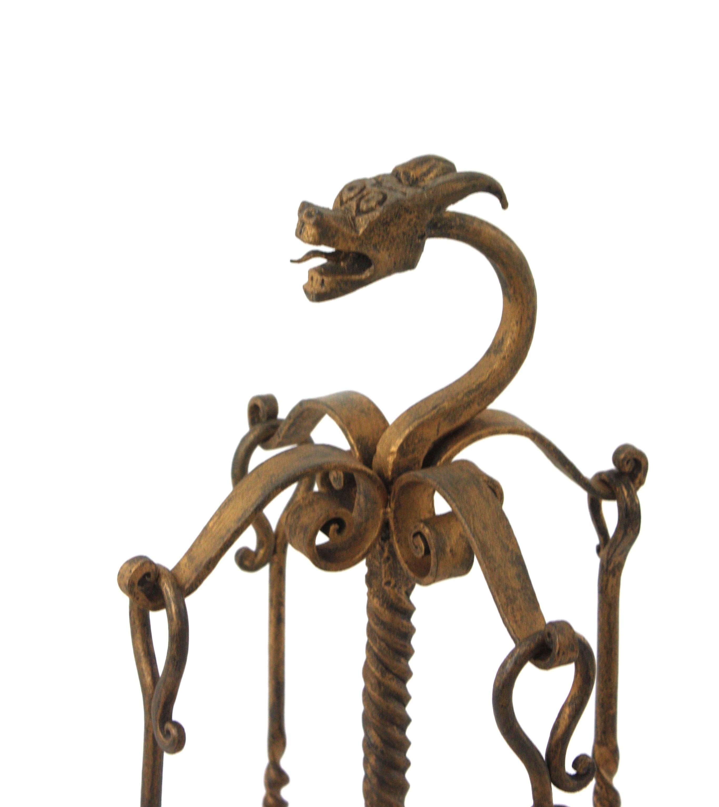 Spanish hand forged iron four-piece fireplace tools set stand with scrolls ornamentation, dragon motif and gilt patinated finish. Spain, 1940s.
This sculptural tools set hangs on a tripod base stand with scrolls ornamentations and a dragon head
