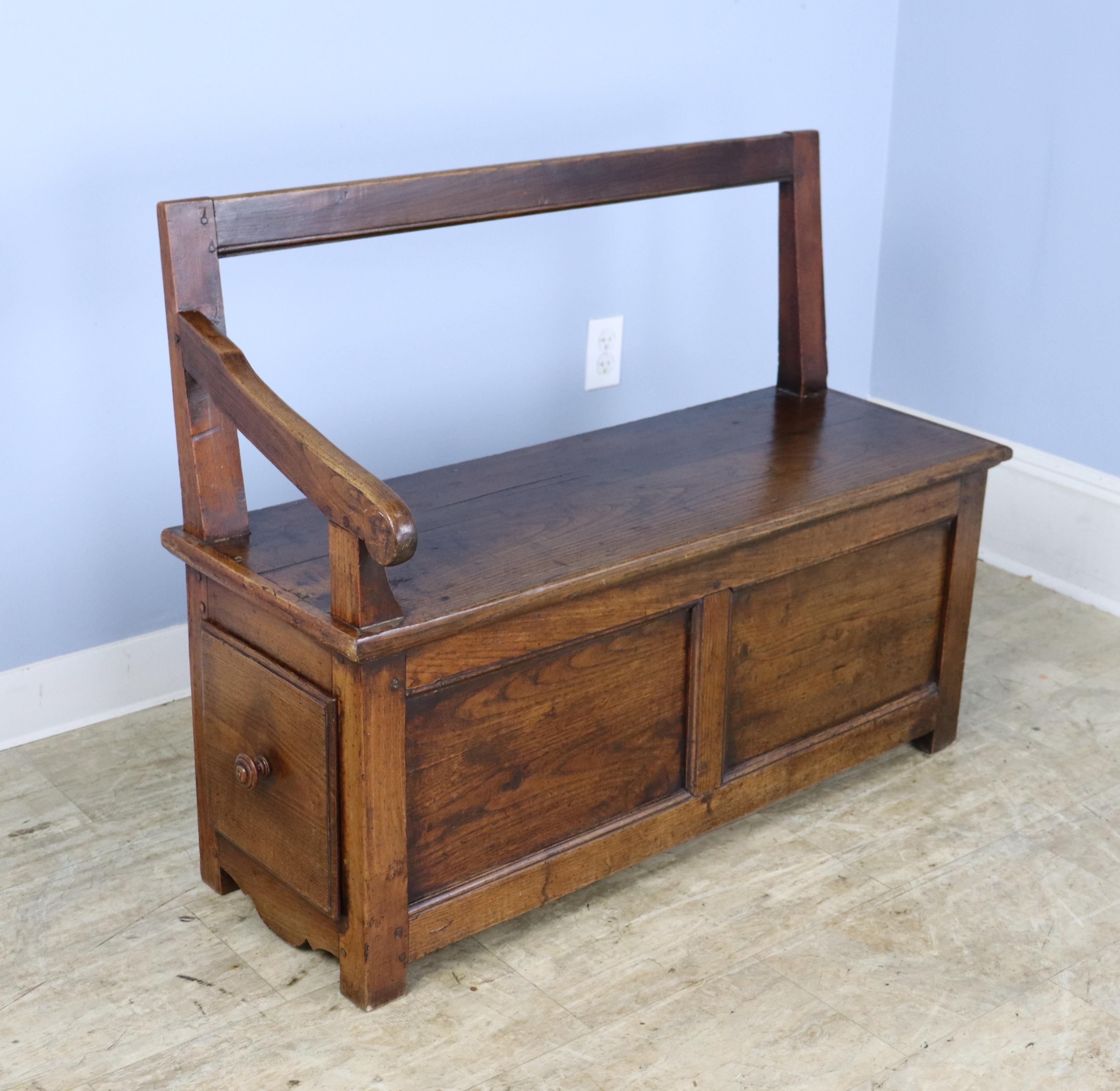This country chestnut bench has very good grain and an elegant appearance. A simple silhouette with a high back and gently sloping single arm. The small drawer at one end of the seat adds a nice design note. Wonderful patina and color. Height