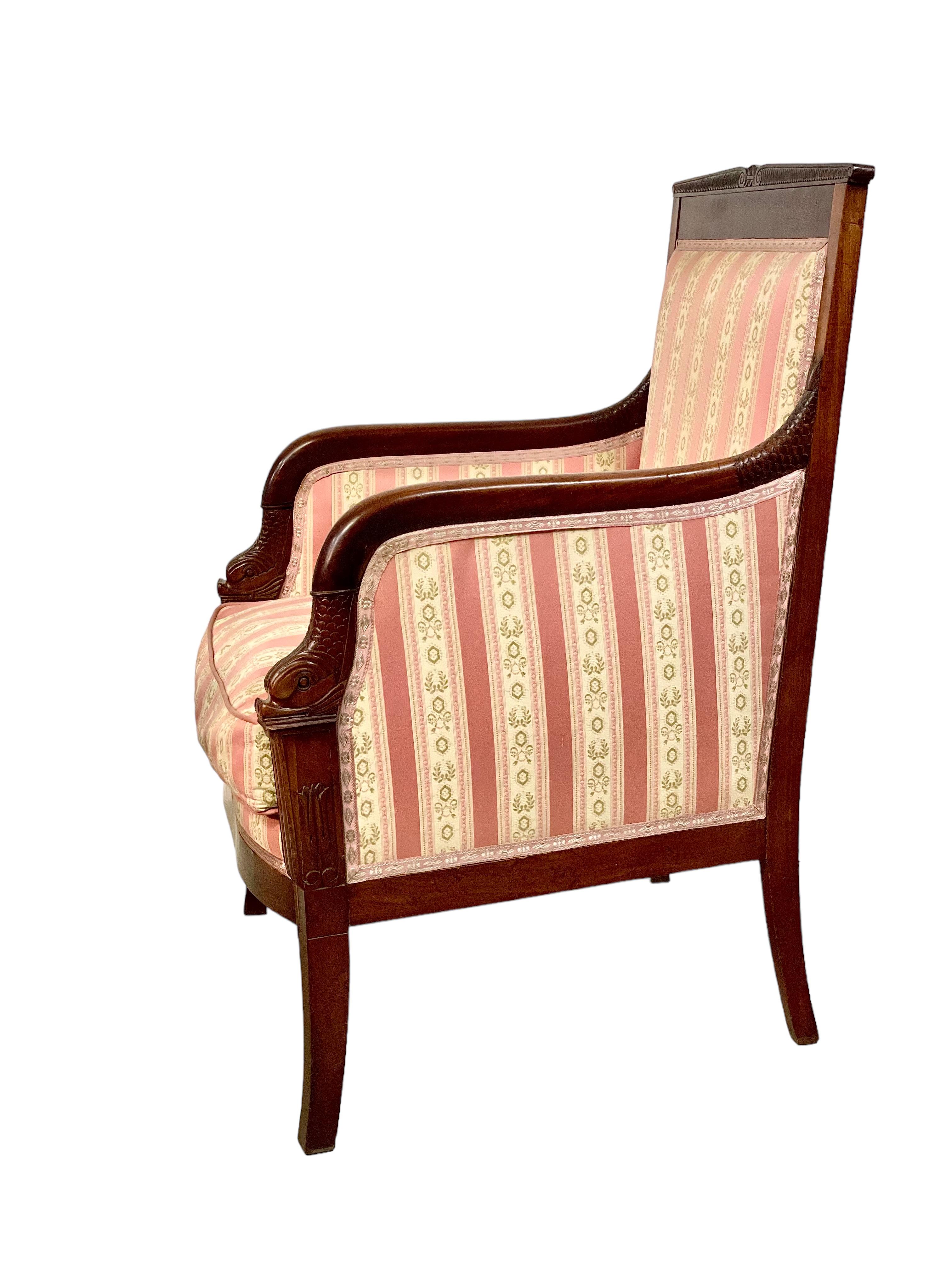 An impressive 'Bergère' armchair in solid wood, dating from the First Empire period (early 19th century) and generously upholstered throughout in alternating stripes of deep pink and cream. This comfortable and stylish chair features a wealth of