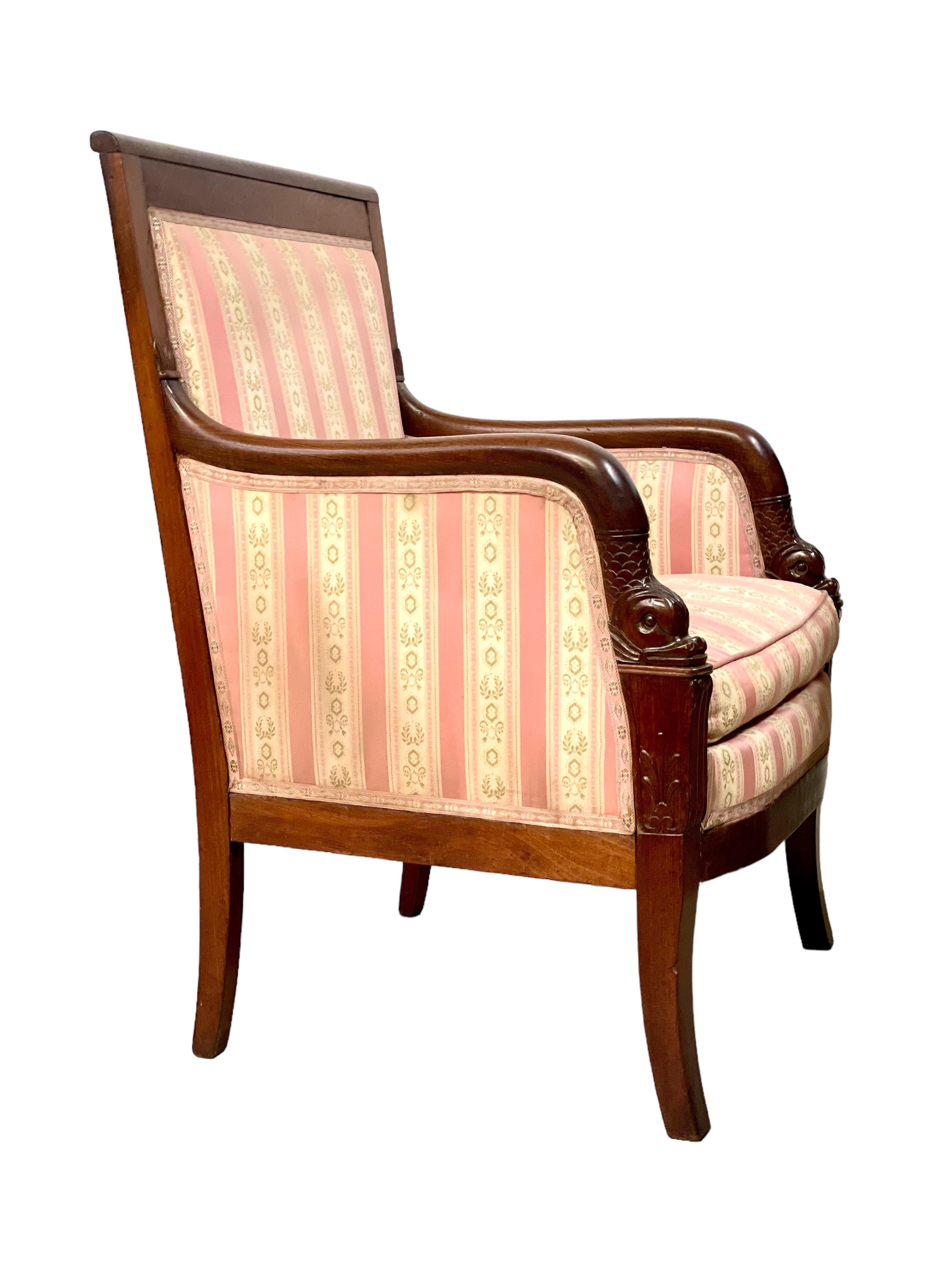 A very fine 'Bergère' armchair in solid mahogany, dating from the First Empire period (early 19th century) and generously upholstered throughout in alternating stripes of deep pink and cream. This comfortable and stylish chair features a wealth of
