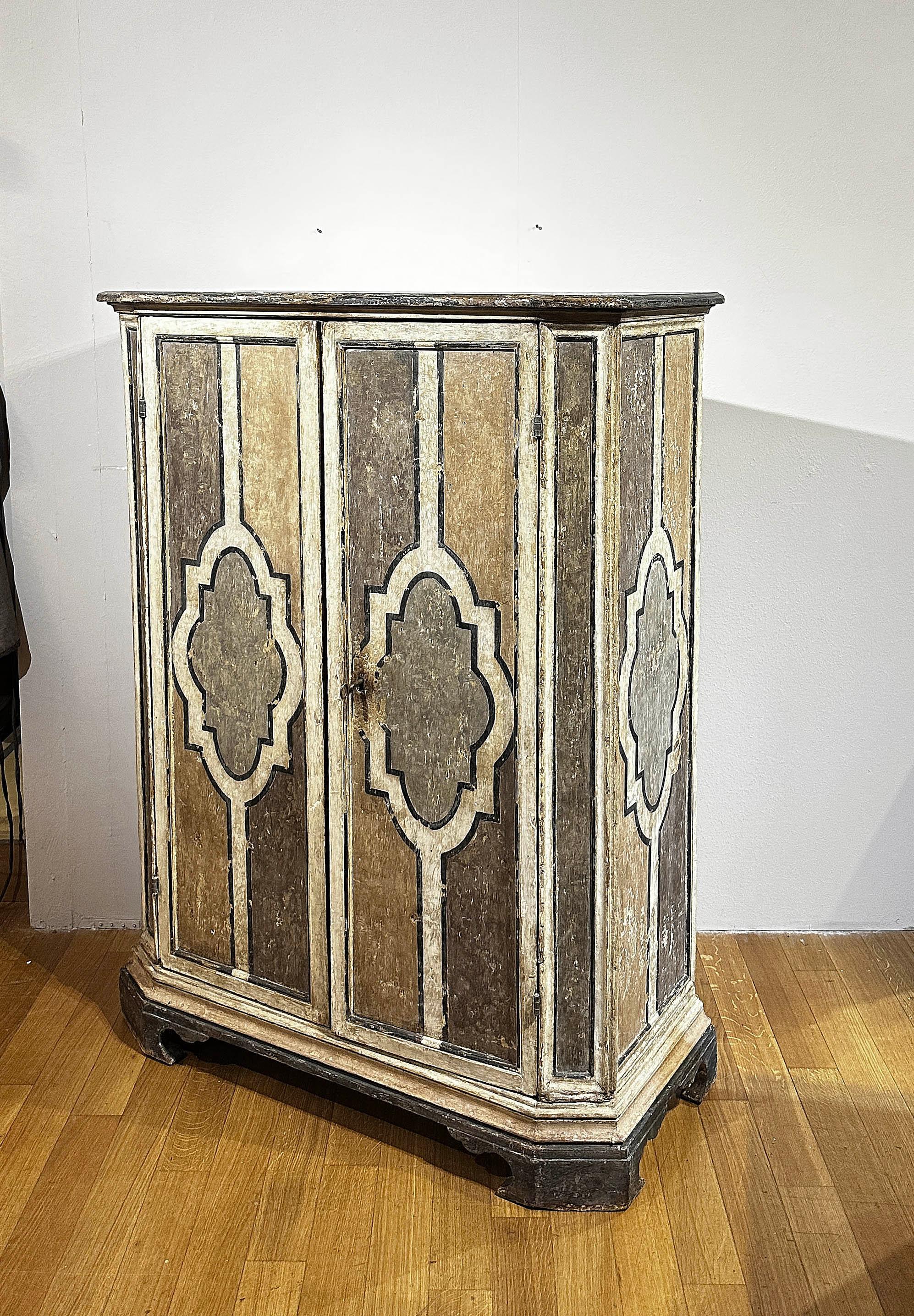 Elegante mobile in abete, finemente intagliato e decorato con tempere nei toni del bianco, giallo, marrone, nero e verde. La struttura presenta angoli arrotondati e piedi a mensola che ne esaltano le linee semplici e raffinate. Dotate di due ante