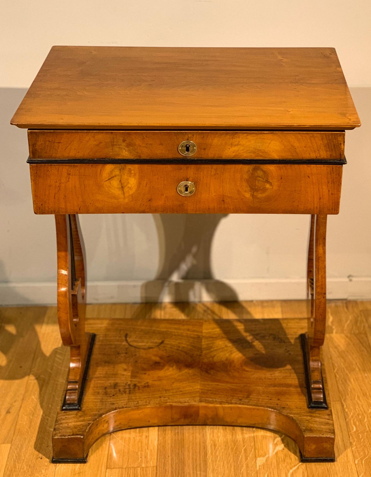 Elegant work table in solid cherry wood with lyre legs with ebonized ropes and gilded bronze studs on the ends. The asymmetrical base is of notable beauty, it was useful for allowing the insertion of a stool or for the legs of the lady who