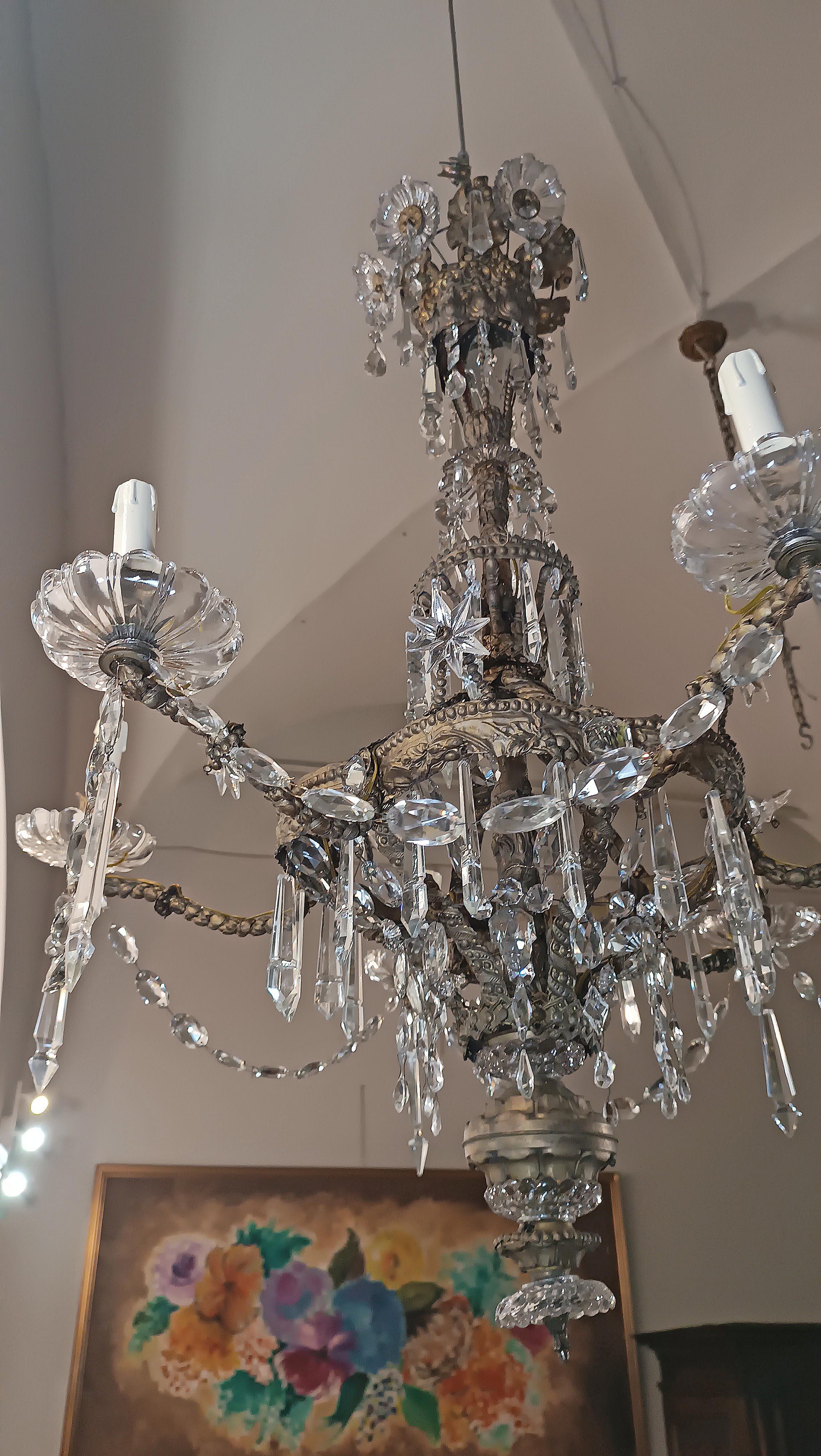 Lustre élégant avec squelette en laiton, cristaux et six lumières. La structure en laiton se distingue par l'alternance de tresses et de décorations végétales, qui rehaussent son élégance. Ce lustre est en outre enrichi de nombreux cristaux,