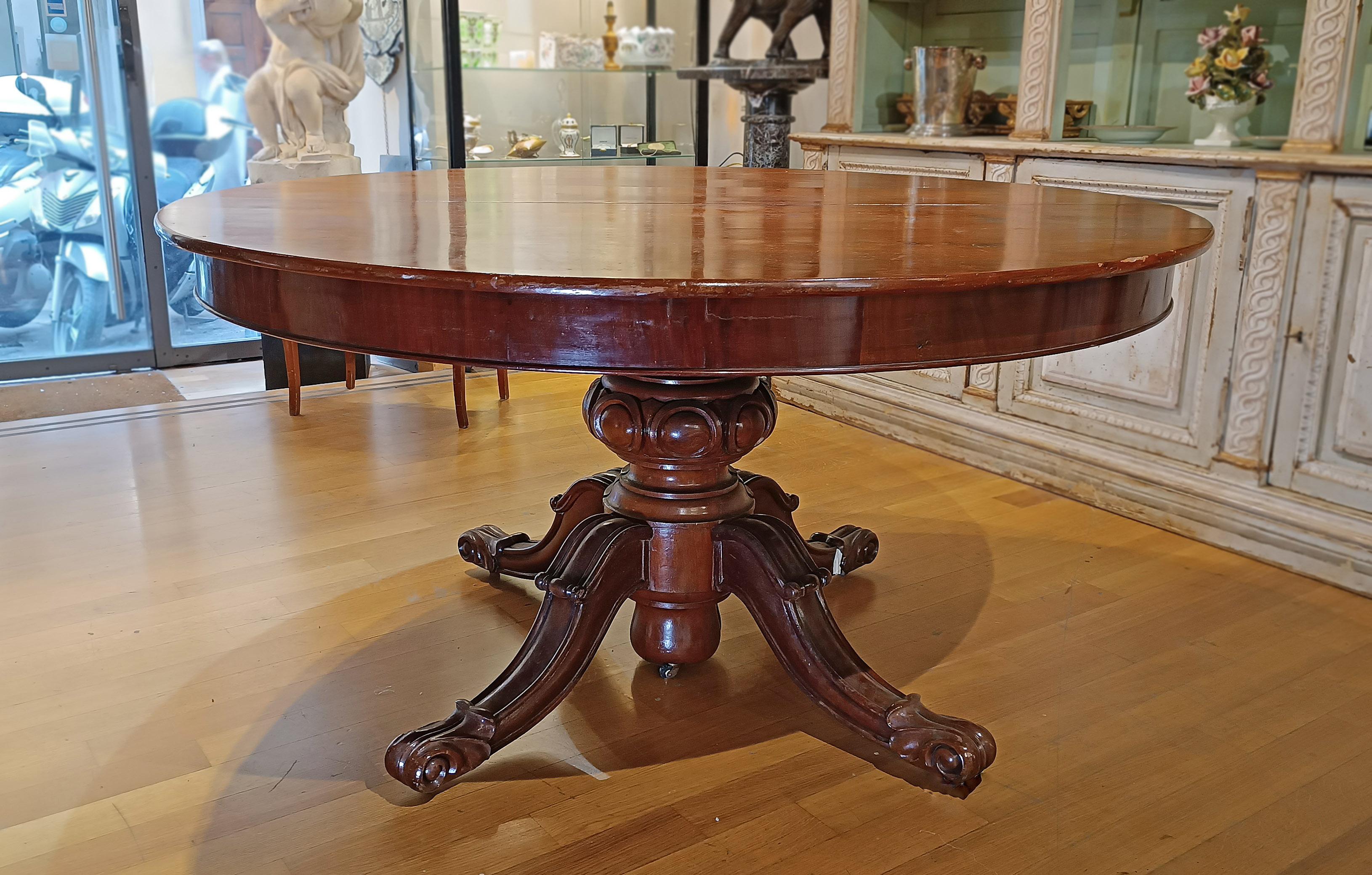 Elégante table ovale en noyer clair massif, avec un plateau lisse et un bandeau sur le dessous. La jambe centrale, tournée de manière experte, se ramifie en quatre pieds décorés de volutes et de terminaisons férales. Le pied central et les quatre