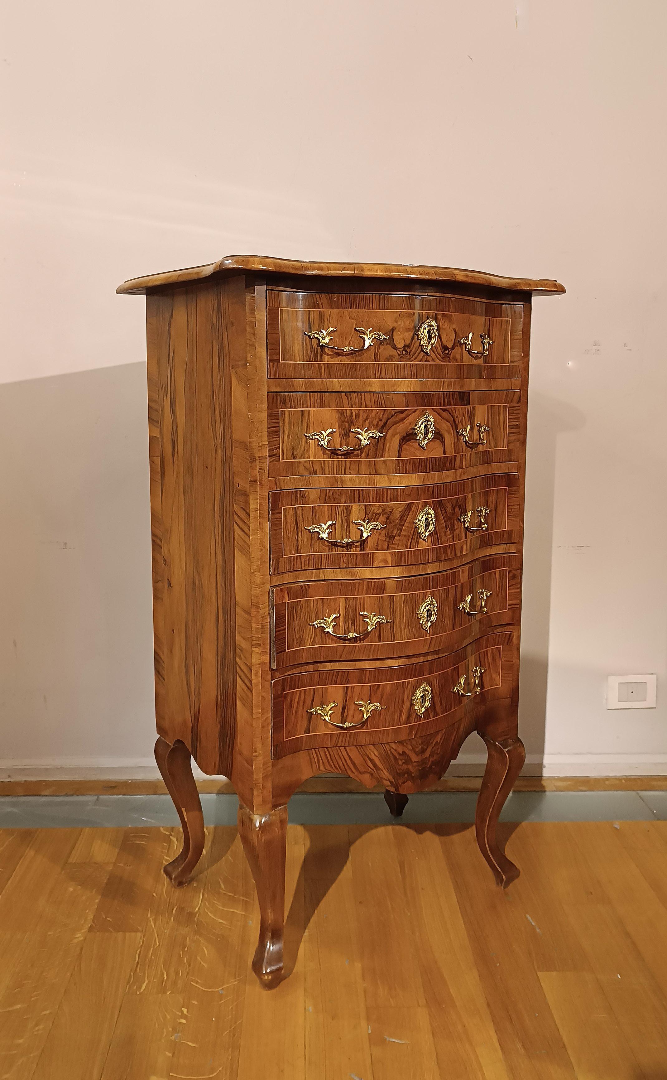 Élégante petite commode en ronce et noyer massif sculpté et plaqué, caractérisée par des pieds galbés et une façade ondulée qui apportent une touche de raffinement. La commode est équipée de cinq tiroirs ergonomiques, idéaux pour le rangement