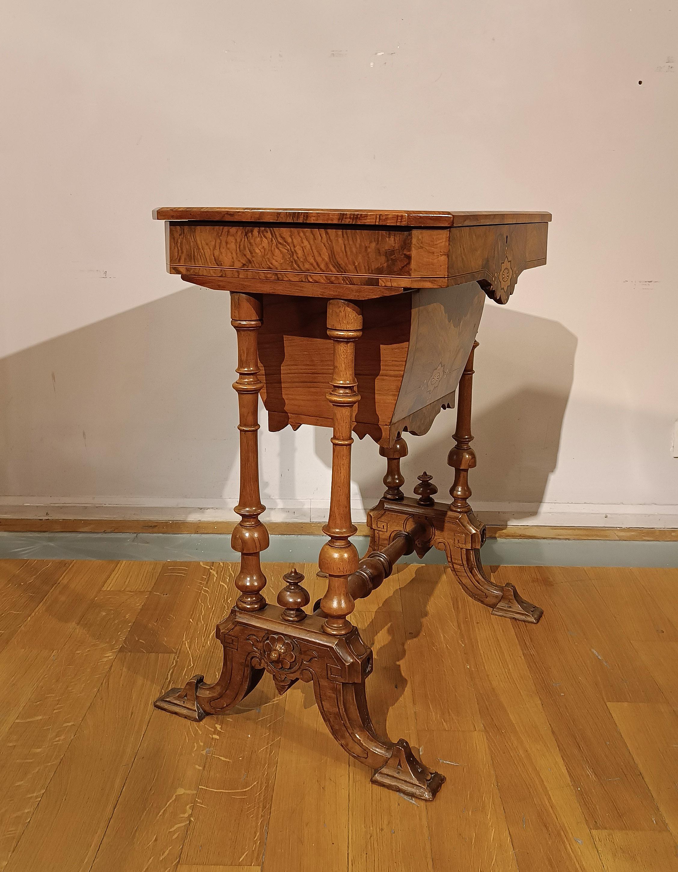 Elegant small work table in walnut root, enriched with carvings and fillets in fruit woods. It is characterized by turned and carved legs, decorated with vegetal and geometric motifs that enhance its aesthetics. The table top can be opened and