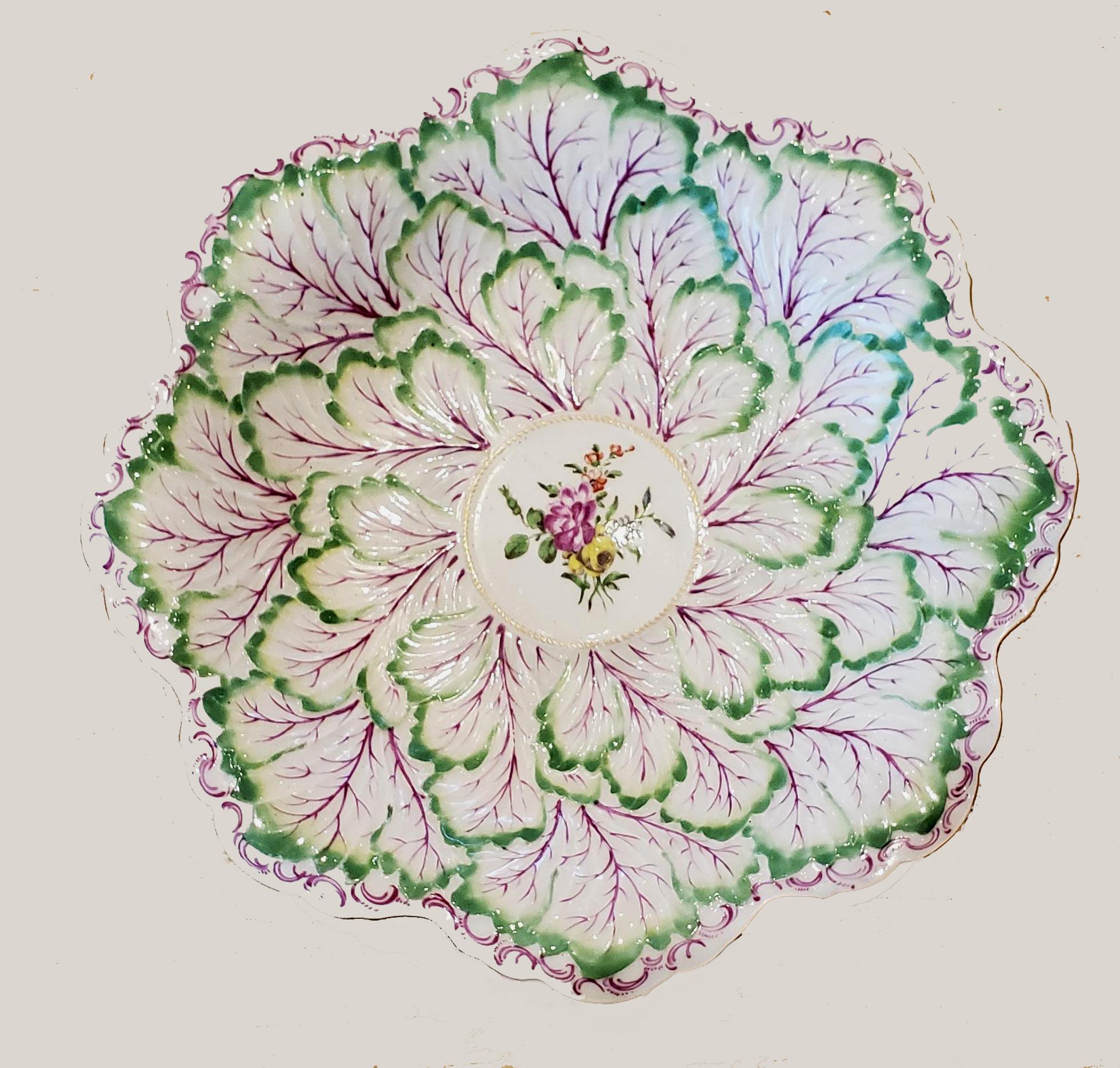 First Period Worcester porcelain rare large leaf and flower dish,
circa 1762-1765.

The large dish with moulded green overlapping leaves with puce veins with a central raised roundel with a polychrome flower bouquet. The rim with puce Rococo