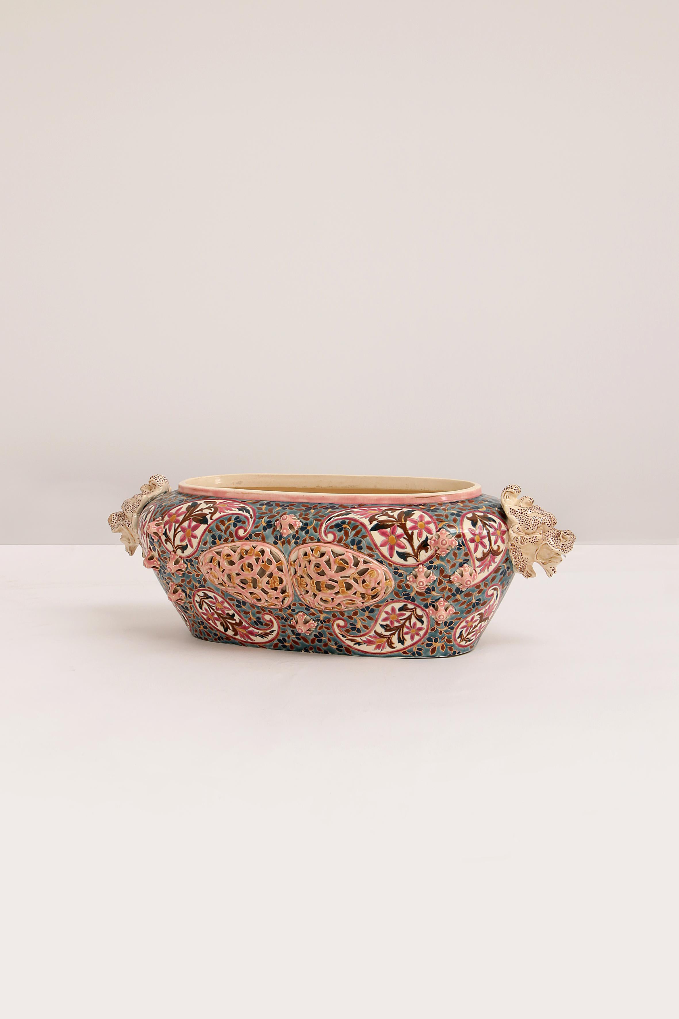 Very rare large Fischer Budapest centerpiece or jardinière painted with intricate brightly colored decoration.

It has colorful handles with a reticulated pattern and three reticulated panels with pink and green borders on the front and
