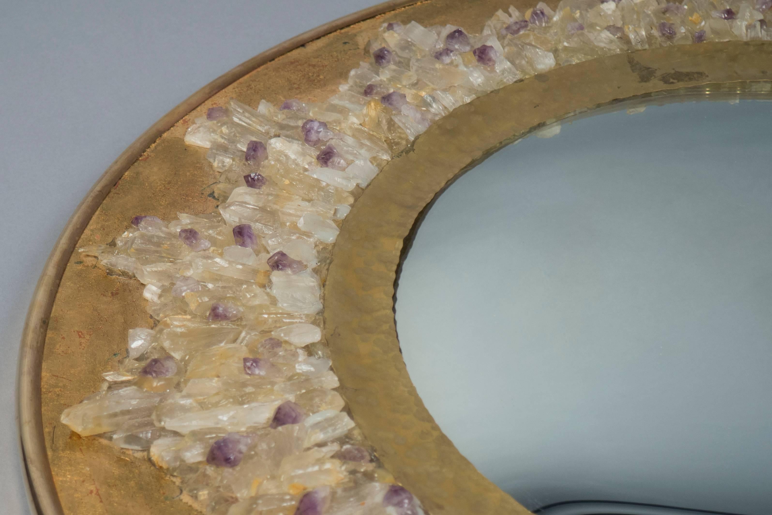 A fish-eye mirror surrounded by a hammered brass band framed by clear and purple quartz crystal clusters on a circular gilded surface.
 