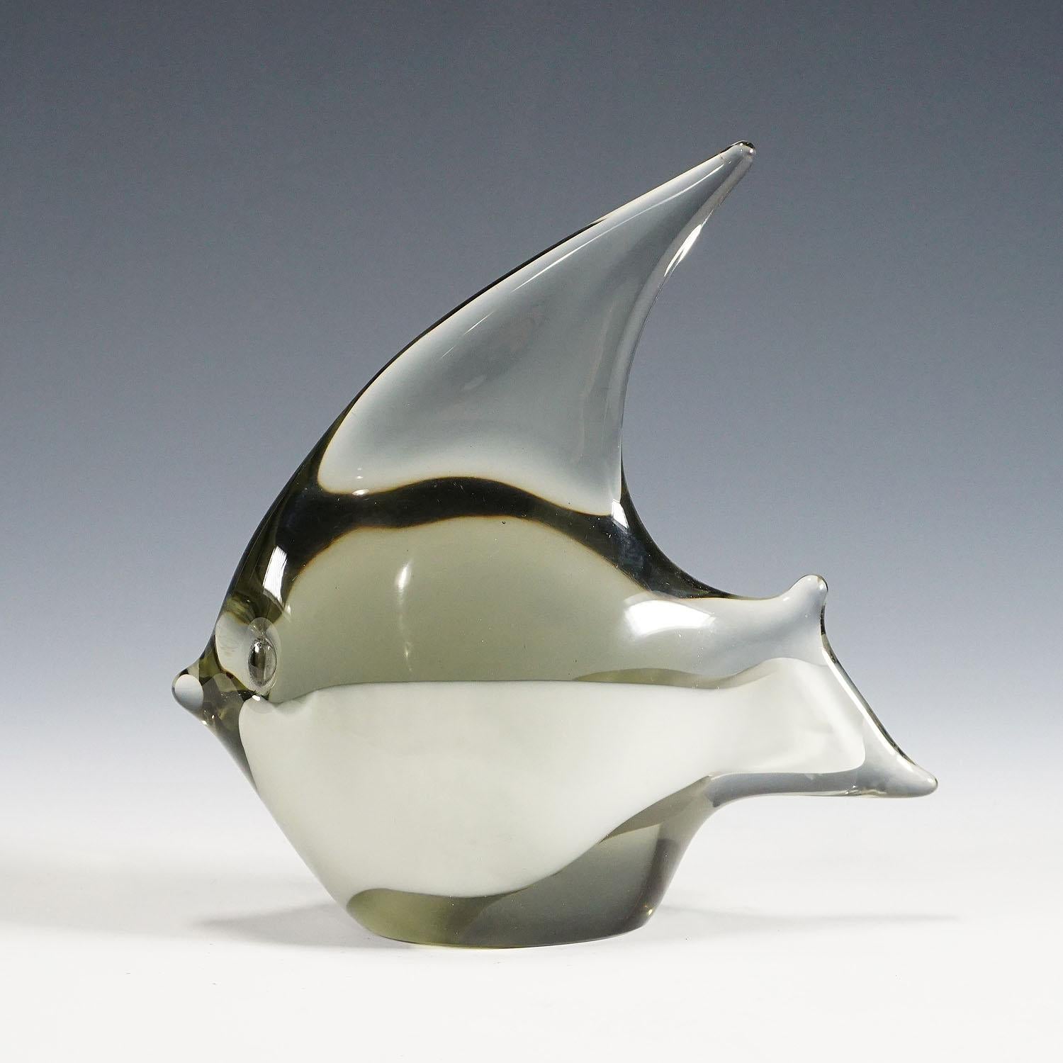 Eine Skulptur eines stilisierten Fisches aus rauchgrauem Glas mit weißem Glasband. Handgefertigt in der Glasmanufaktur Gral, Deutschland. Entworfen von Livio Seguso um 1970. Eingeschnittene Signatur des Künstlers (LS) auf dem Sockel.

Livio Seguso