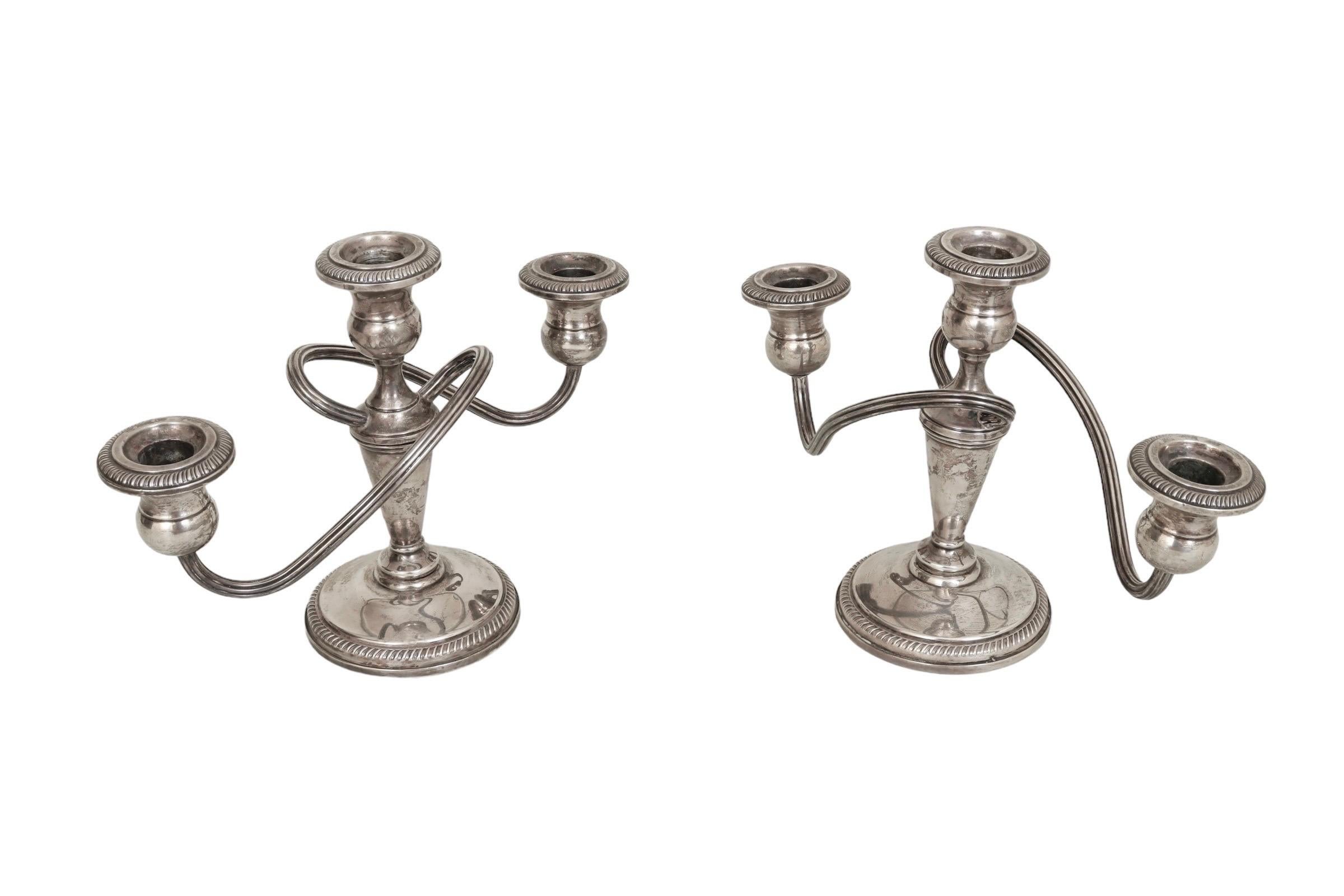 Pareja de candelabros ponderados de plata de ley estilo Imperio de la década de 1930, fabricados por Fisher. Una columna central torneada sostiene dos brazos reticulados retorcidos, todo rematado con apliques reticulados. Marcado 