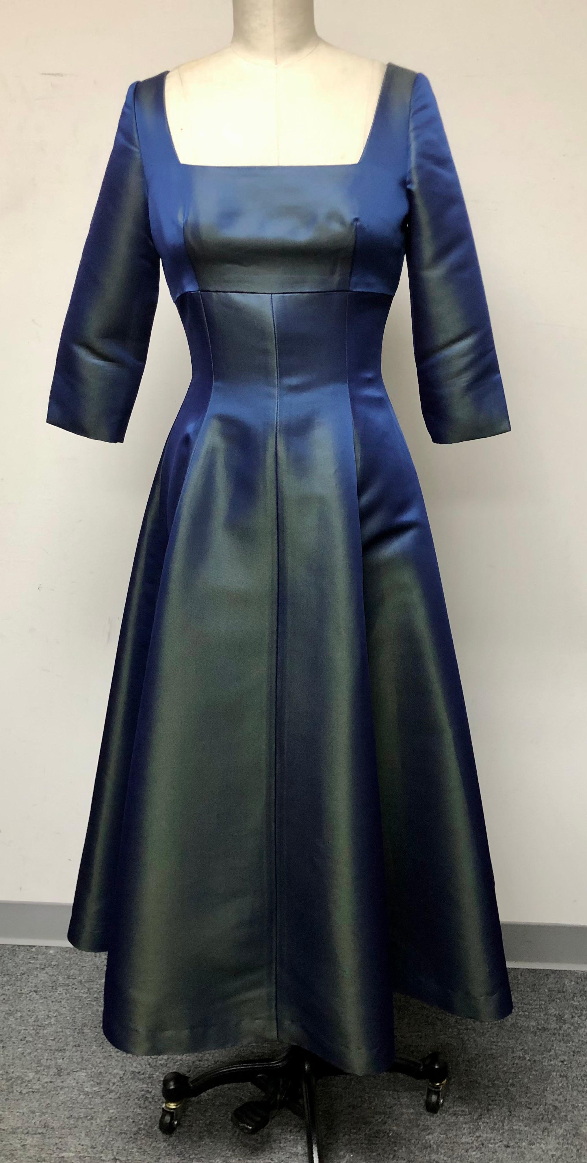 Vestido entallado con cuello cuadrado y manga 3/4. Originalmente diseñado para Adele y llevado por ella. Ideal para fiestas y bailes, un auténtico vestido de fiesta. El tejido iridiscente de satén grueso azul y verde le da un aire festivo. Mostrado