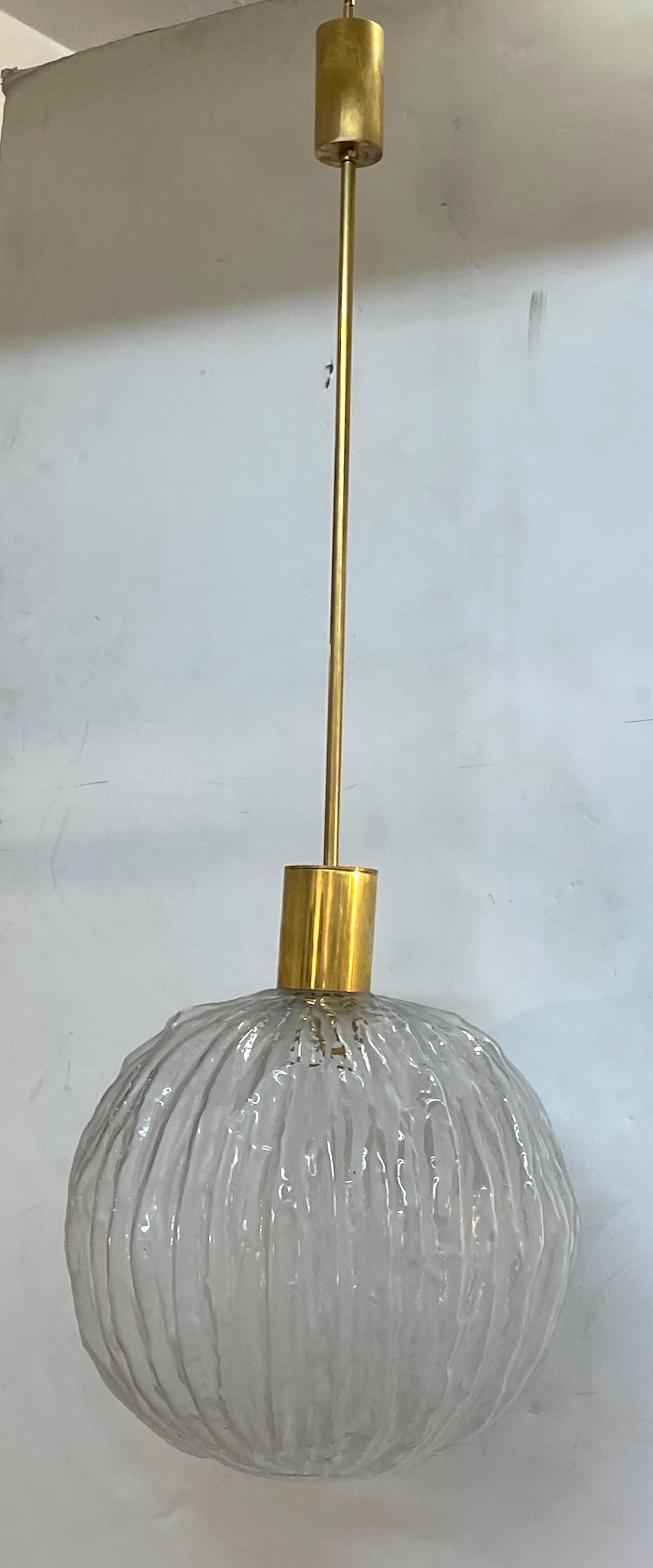 Shown are two of five available Italian 1960s pendant lights by designer Angelo Brotto. Each pendant is comprised of a brass rod with original ceiling canopy at the top. At the bottom is a machine socket cover that supports the molded glass globe