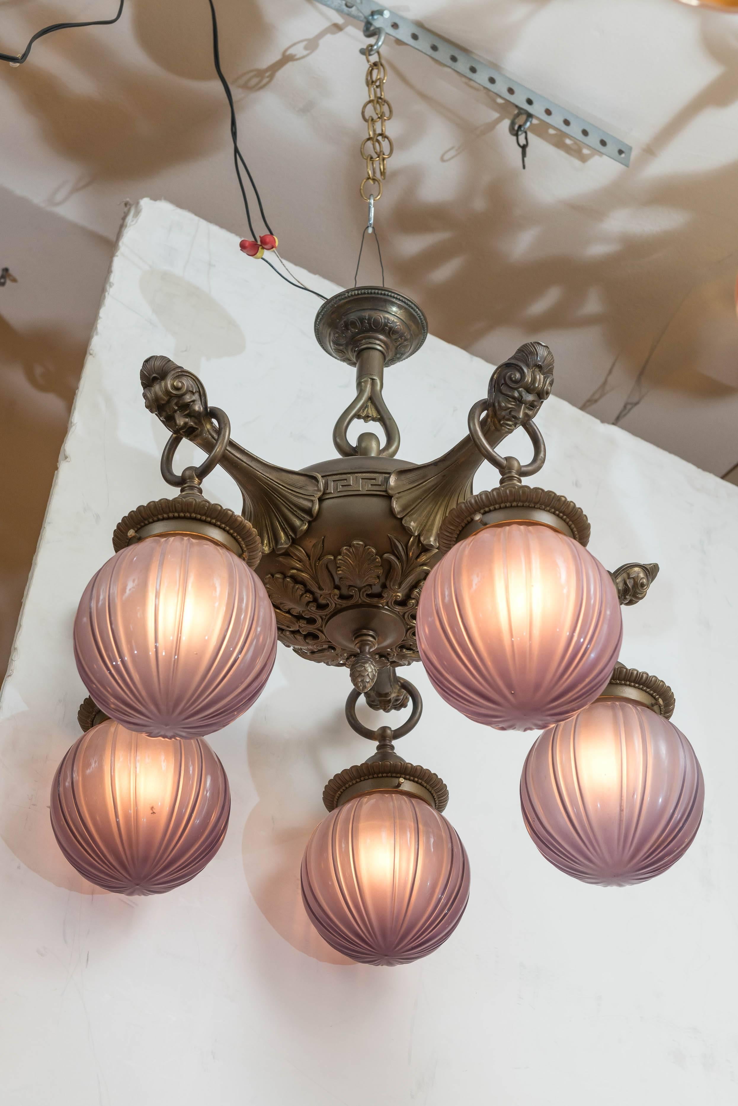 What a neat chandelier we are offering. The body has fleur de lys, and each arm has a face at the tip. The shades are really extraordinary. When the frosted glass is unlit the shades are a very light purple, and lit the purple becomes less