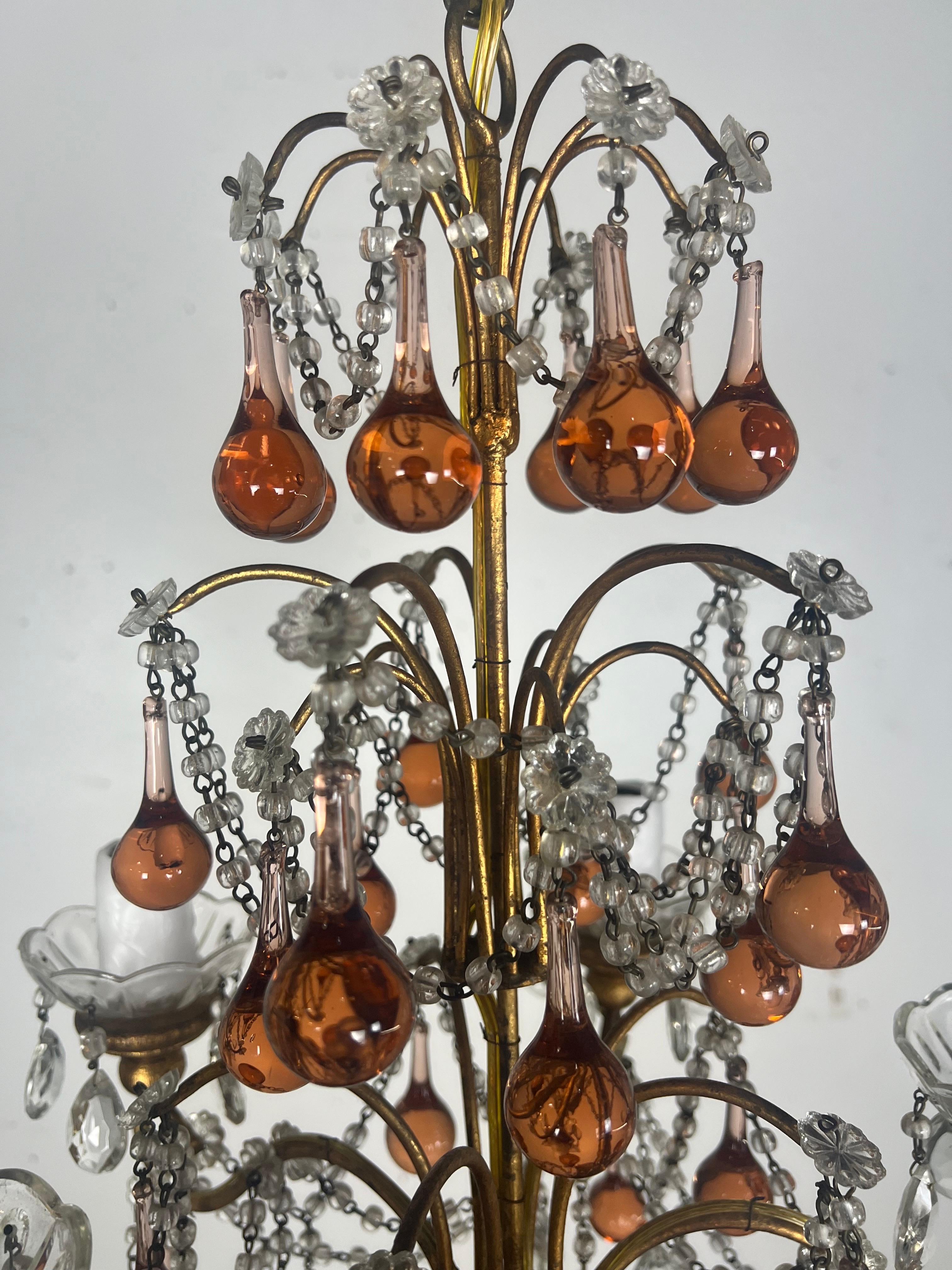 Araña de cinco luces de cuentas de cristal italiano.  La araña tiene un diseño escalonado con varios niveles de decoración y apliques de luz.  Presenta abundantes gotas de vidrio y cristal, incluidos cristales transparentes y en forma de lágrima de