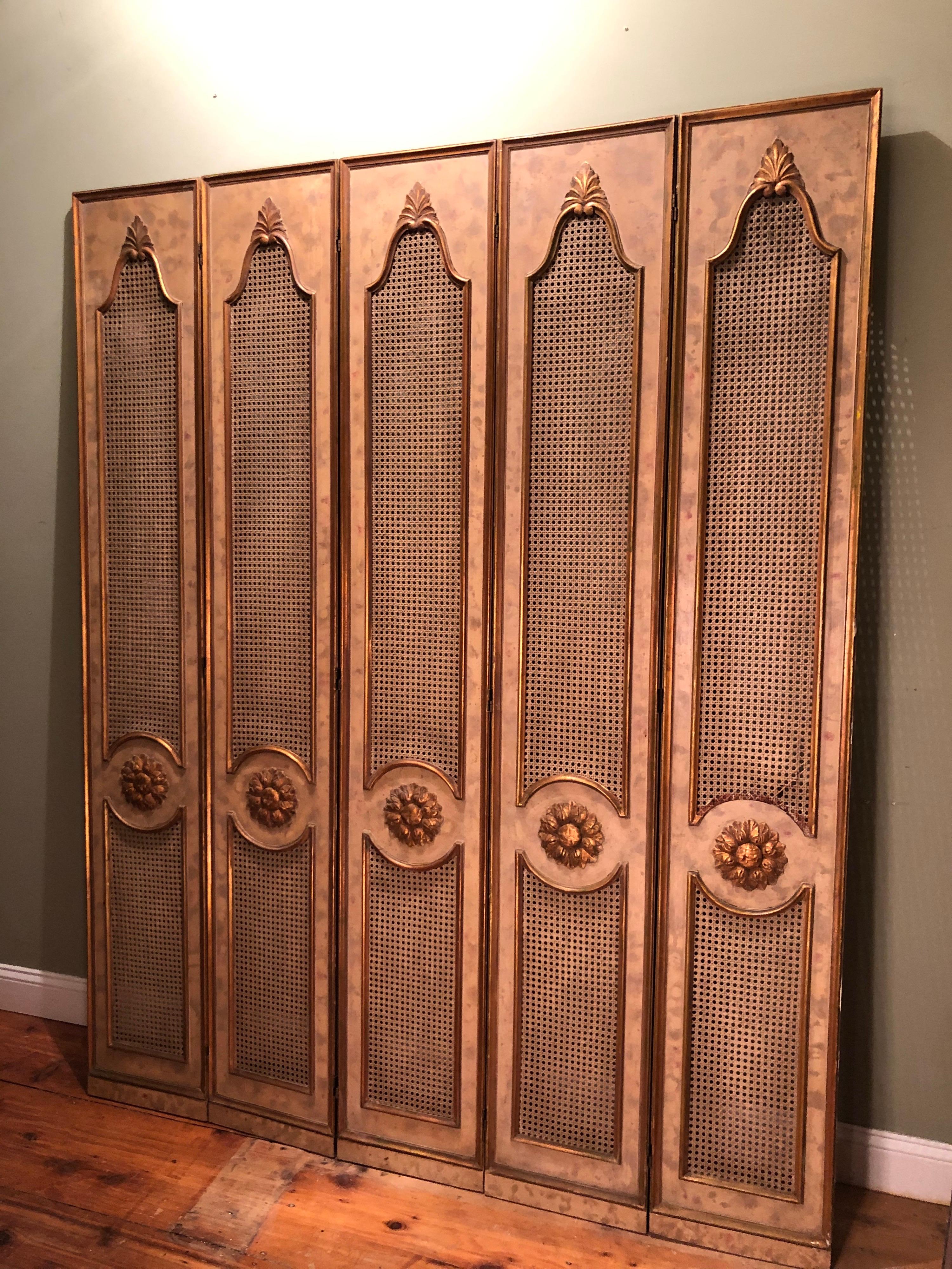 Five-paneled French gilt folding screen. Perfect for privacy or for covering up an area. Gorgeous carved wooden gilt design with caning and hand painted background. Reverse side has a different pattern with some fabric. One outer panel has damage to