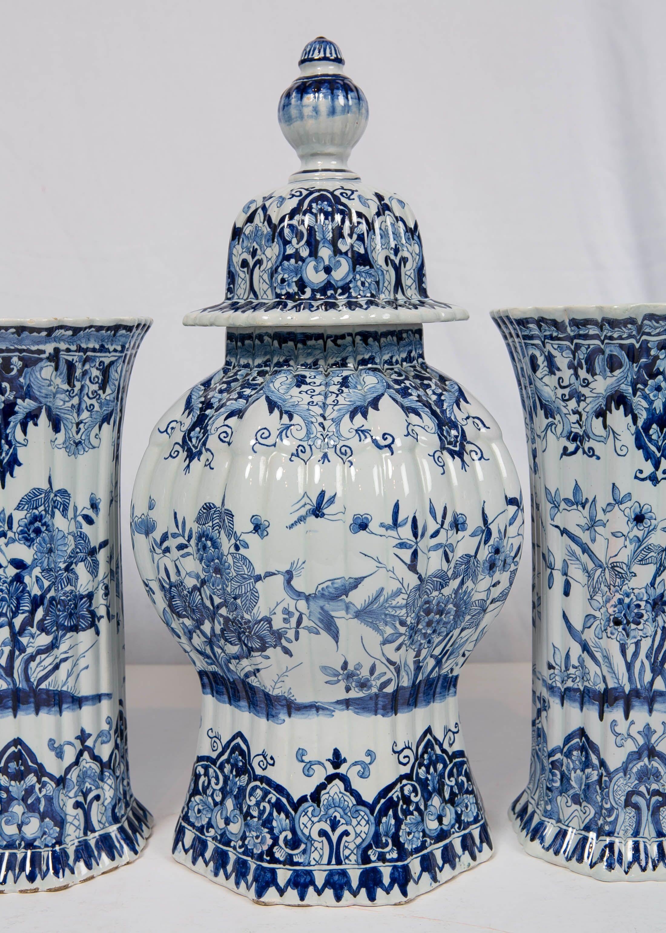 A five-piece French blue and white garniture in the style of delft made by the highly esteemed French company Samson et Cie, in the first quarter of the 20th century. The vases are octagonal, and ribbed. The scene on the vases shows a bird in