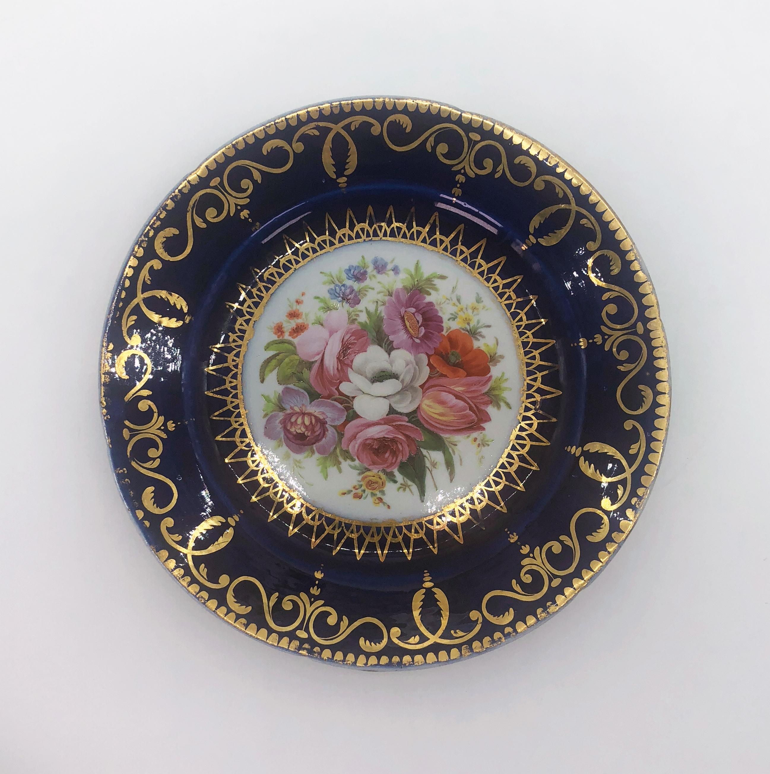 Five Regency side plates by Coalport with hand painted panels of flowers, circa 1805. Cobalt borders support a gilded band of interlocking scrolls and finials with a gold dentil border. Hand painted panels of floral bouquets in the manner of the