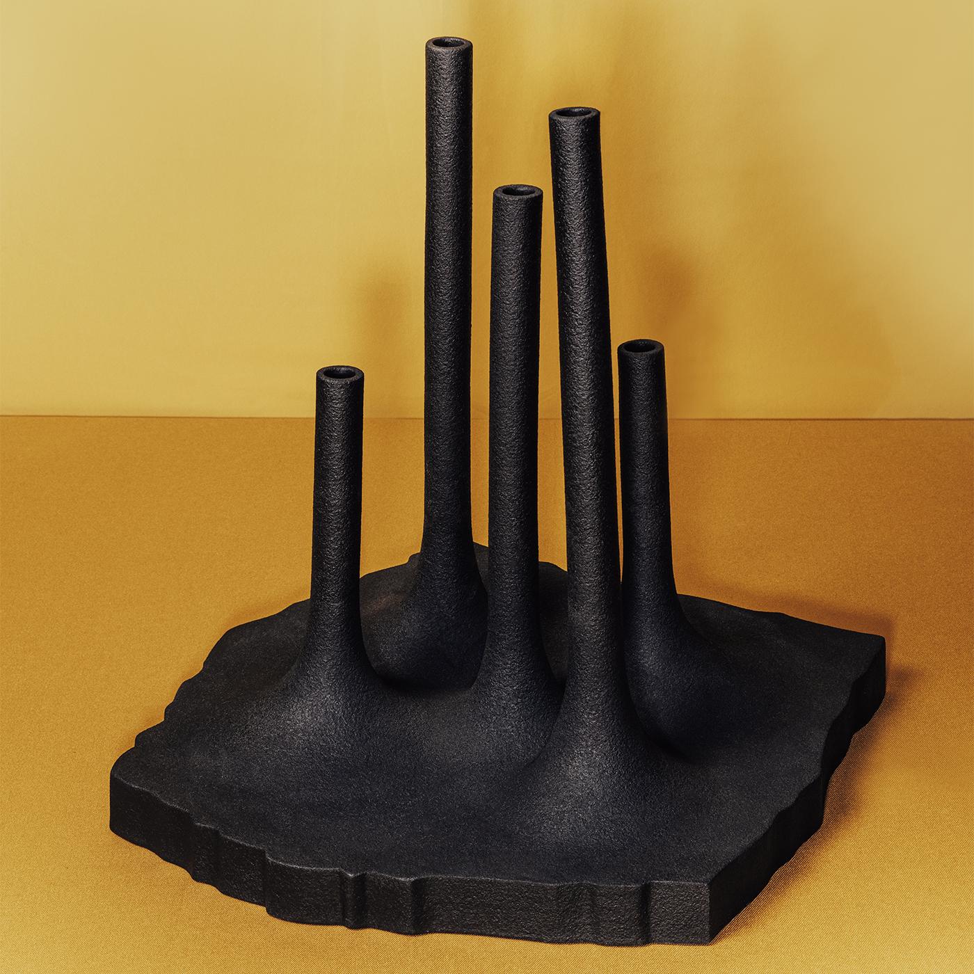 Questo vaso presenta una composizione unica di cinque steli cilindrici di diverse altezze che si ergono da una base strutturata che funge da serbatoio d'acqua. La superficie viene prima rivestita con un morbido smalto nero opaco e poi arricchita con