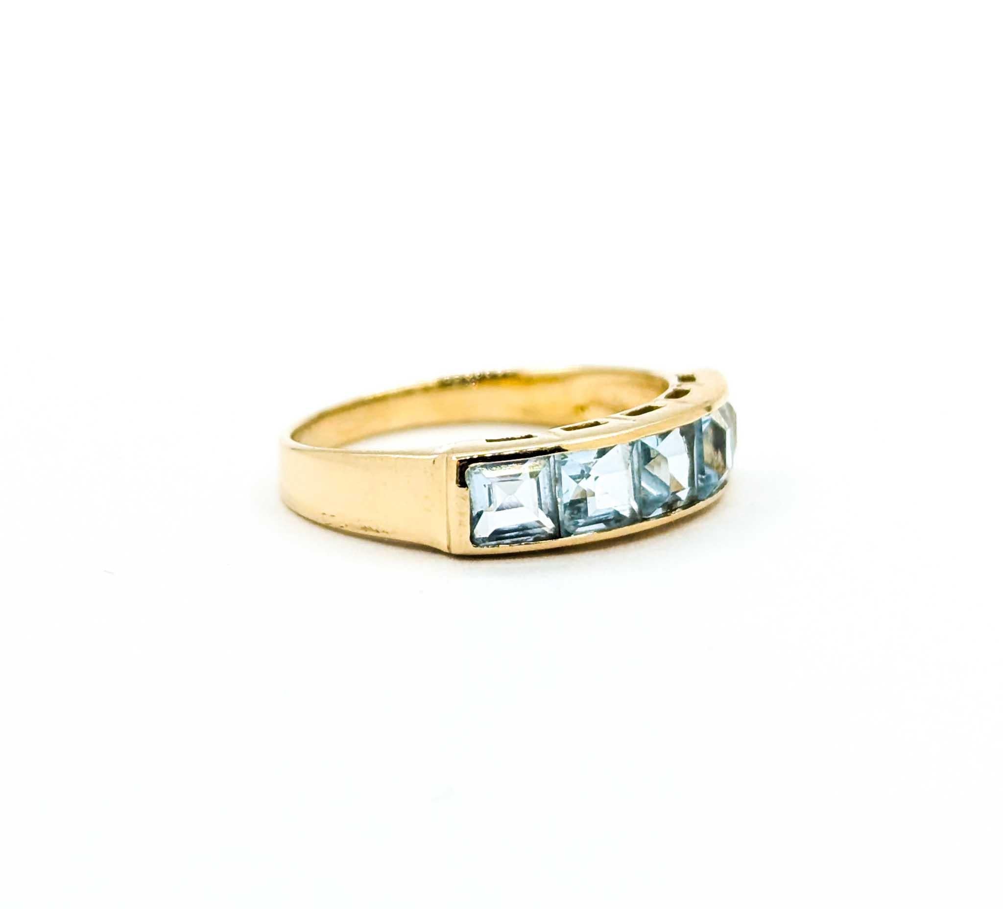 This vintage band features five square-cut sky blue topaz gemstones, weighing a total of approximately 1.25 carats. The stones are channel-set across the top, creating a sleek line of soft blue sparkle against warm 14k yellow gold. Its low-profile