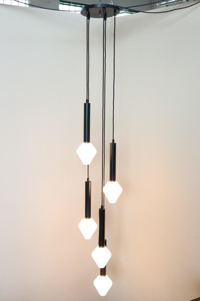 We present this particular chandelier with a unique cascade design, Italian production circa 60s/70s. The cascade effect is structured in five levels with a black lacquered metal structure, a gold brass detail and white satin glass lampshades.

This