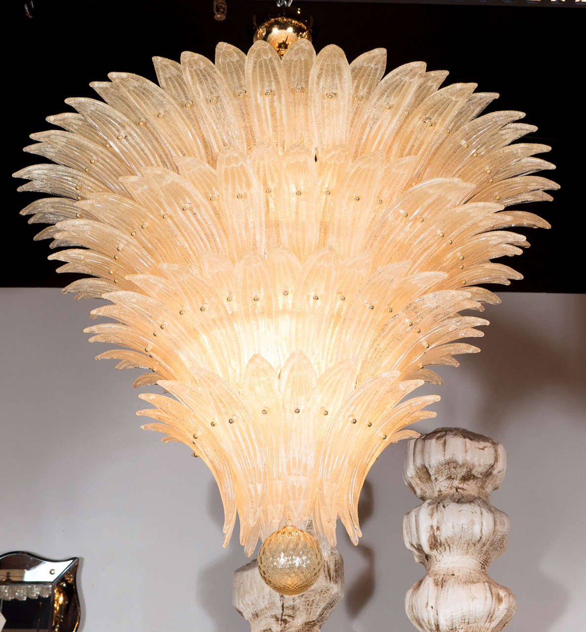 This exquisite Palma chandelier consists of five tiers of individually hand blown Murano glass stylized palm fronds in an iridescent Champagne color that are adhered to its brass frame in an alternating fashion on each tier that form a descending