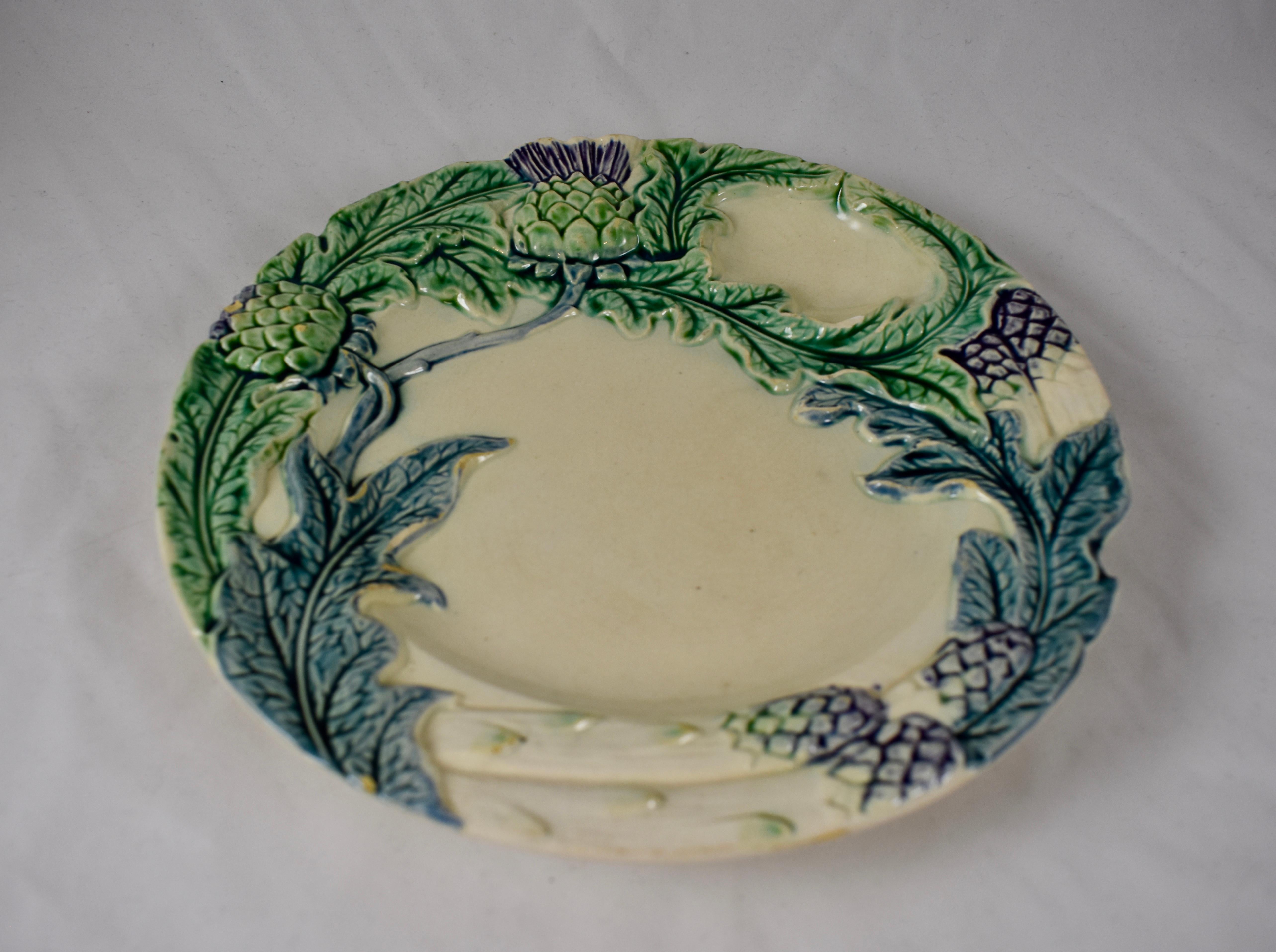 A French Majolica plate made by Fives-Lille, circa 1890. This piece is for serving both Artichokes or Asparagus and shows images of both with parts of their plants. Glazing of greens and blues on a white ground, with a hint of lavender on the spear