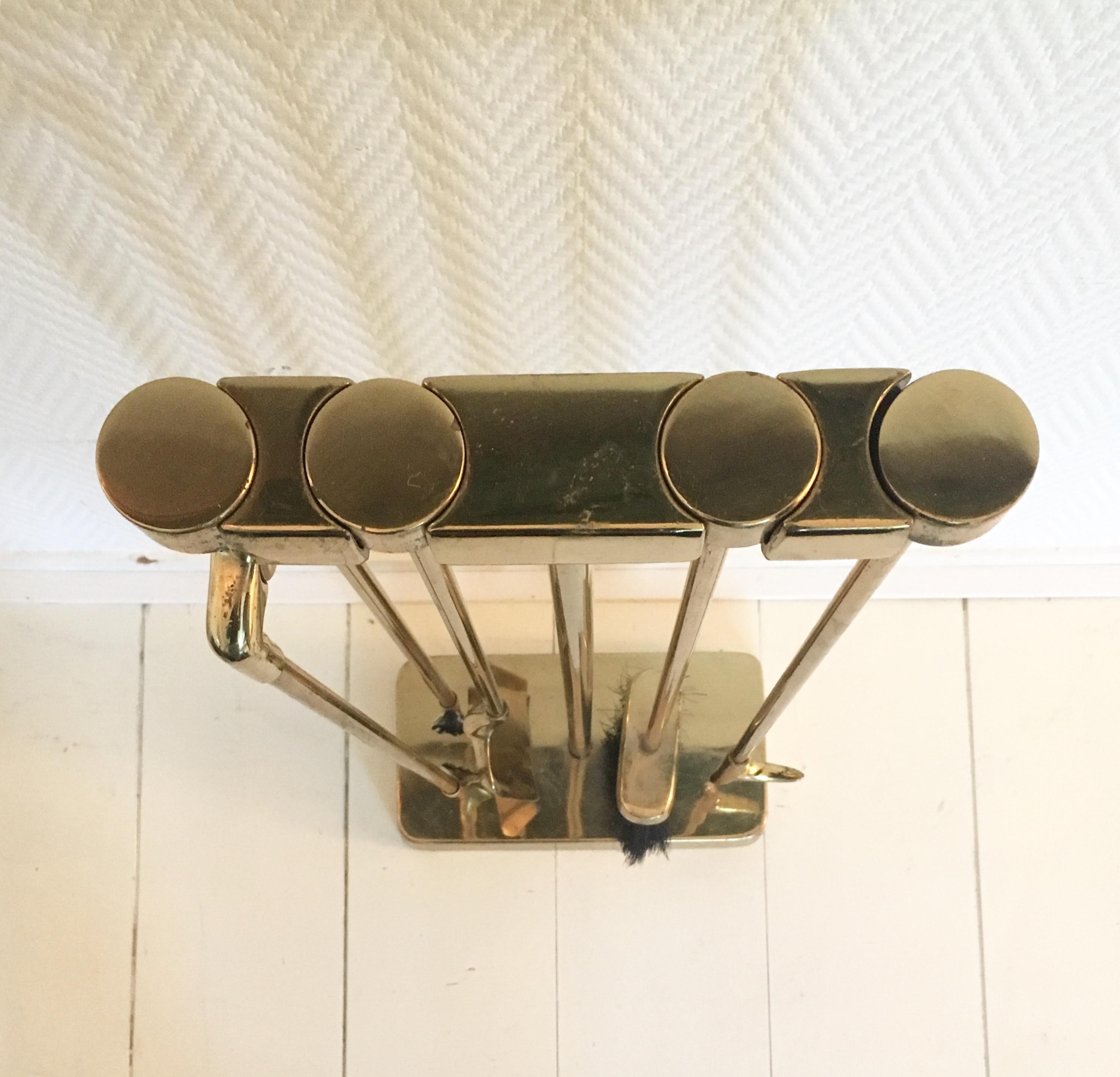 A very nice four-piece set of brass fire tools on a stand. Each of the tools features a round head that insets into the top of the stand. Each of the slots on the top of the stand is marked to indicate the tool placement (Shovel, Brush, Poker,