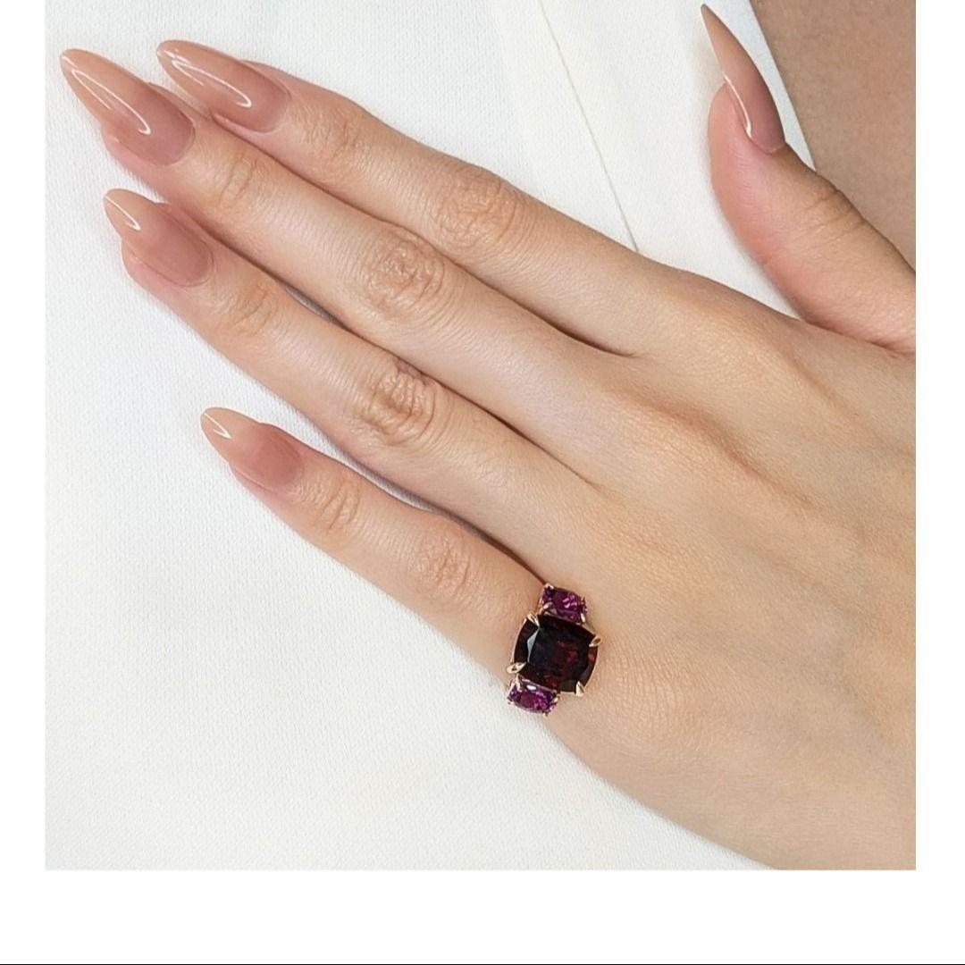 Dieser prächtige Ring aus 18 Karat Roségold trägt in seiner Mitte einen atemberaubenden Granat im Kissenschliff von 5,8 Karat, der tiefe, dunkelrote Farbtöne ausstrahlt und Raffinesse verströmt. Flankiert von zwei auffälligen Amethysten im