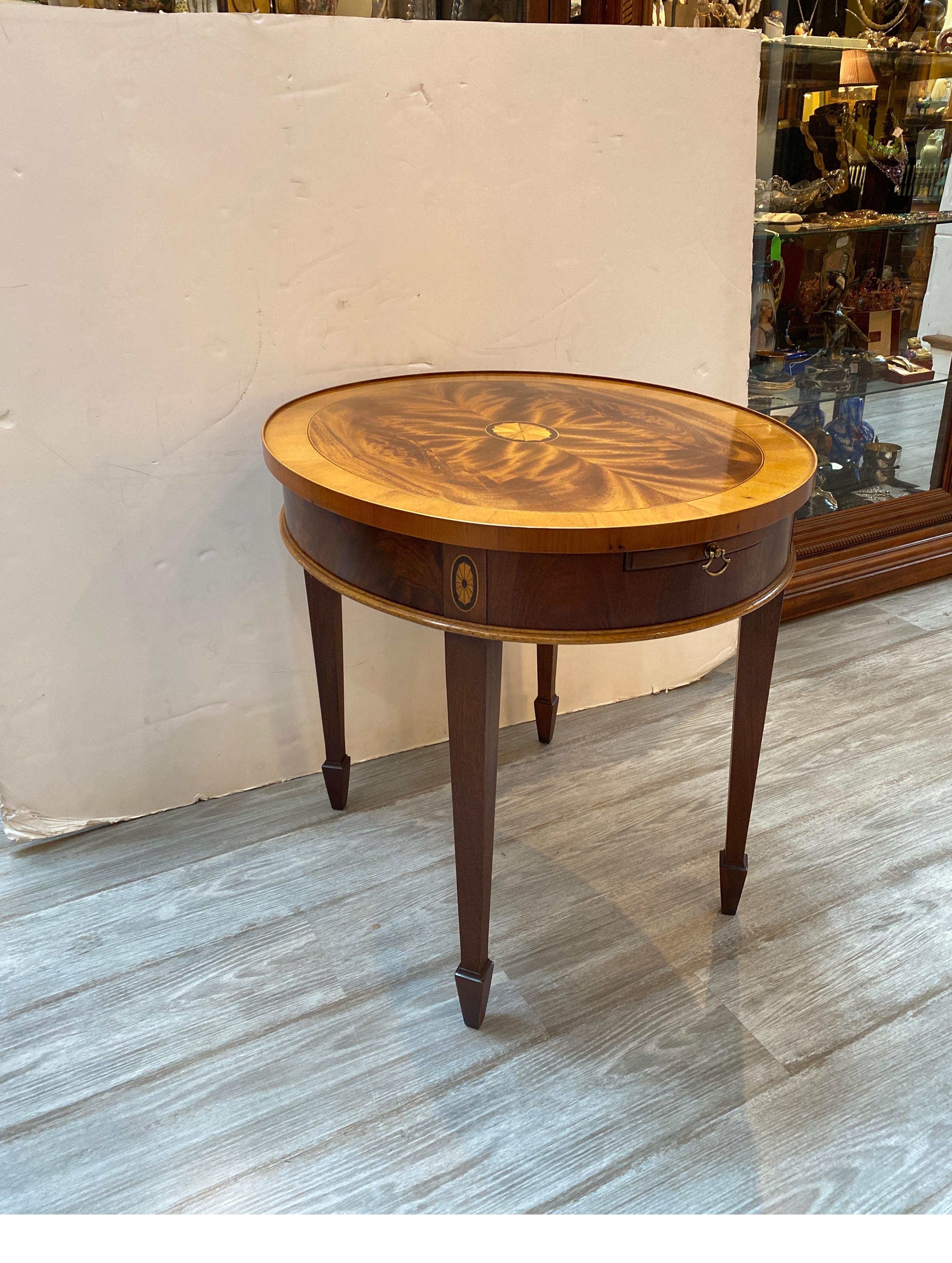 Elegant oval flame mahogany table with candle pull out shelf by Hekman. The highly figurative top with center satinwood medallion The tapering legs with inlay at the top. The front with a mahogany pull out tray.