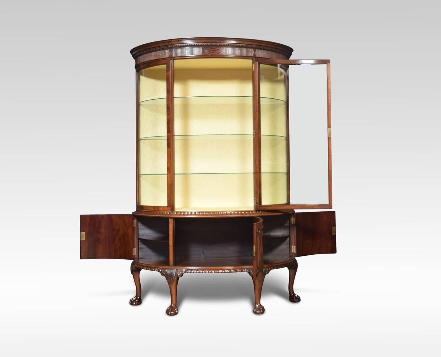 Early 20th century flame mahogany bow fronted display cabinet, having egg and dart moulded cornice, above large glazed door opening to reveal watermark silk upholstered interior with three glazed shelves. The base section fitted with three cupboard