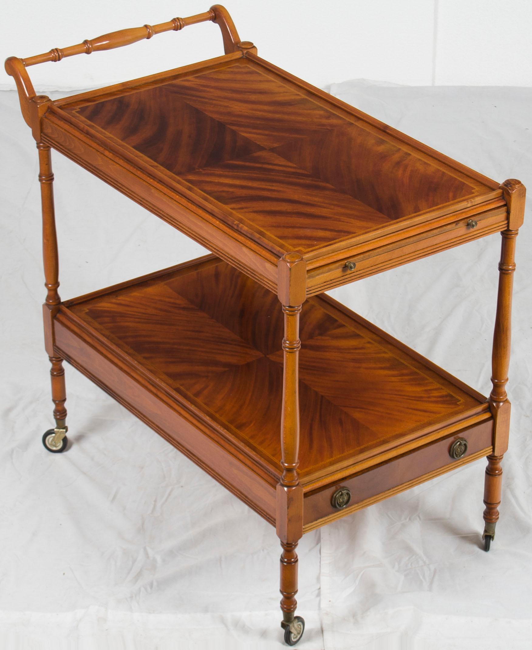 This unique antique tea cart was made in England, circa 1960. It has two-tier for serving or display and is decorated with fluted molding and satinwood inlays. While the original use for a tea cart such as this is quite obvious, today they can be