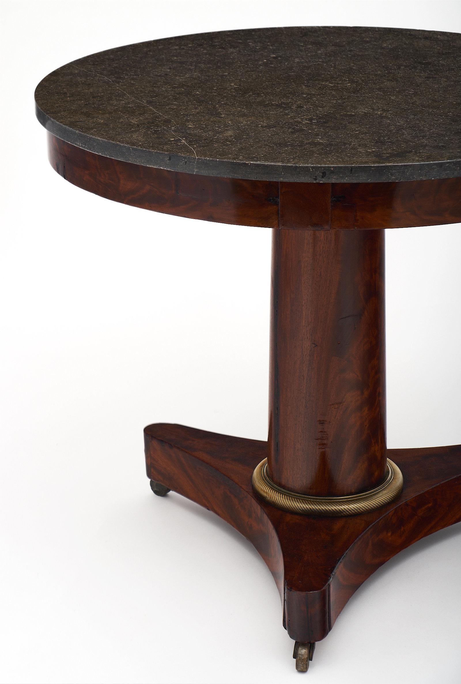 Empire style flamed mahogany gueridon with a gray marble top and bronze hardware. The dark color of the marble is very elegant, and the French polish finish of the base adds a sophisticated luster. This piece is supported by casters. We love the