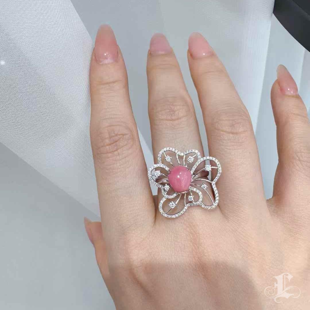 Ein strahlendes Fest der natürlichen Schönheit: Im Mittelpunkt dieses außergewöhnlichen Rings steht eine seltene 3,35-karätige Muschelperle in einem leuchtenden Flamingo-Rosa, die ein ausgeprägtes Flammenmuster aufweist - ein optisches Wunder, das