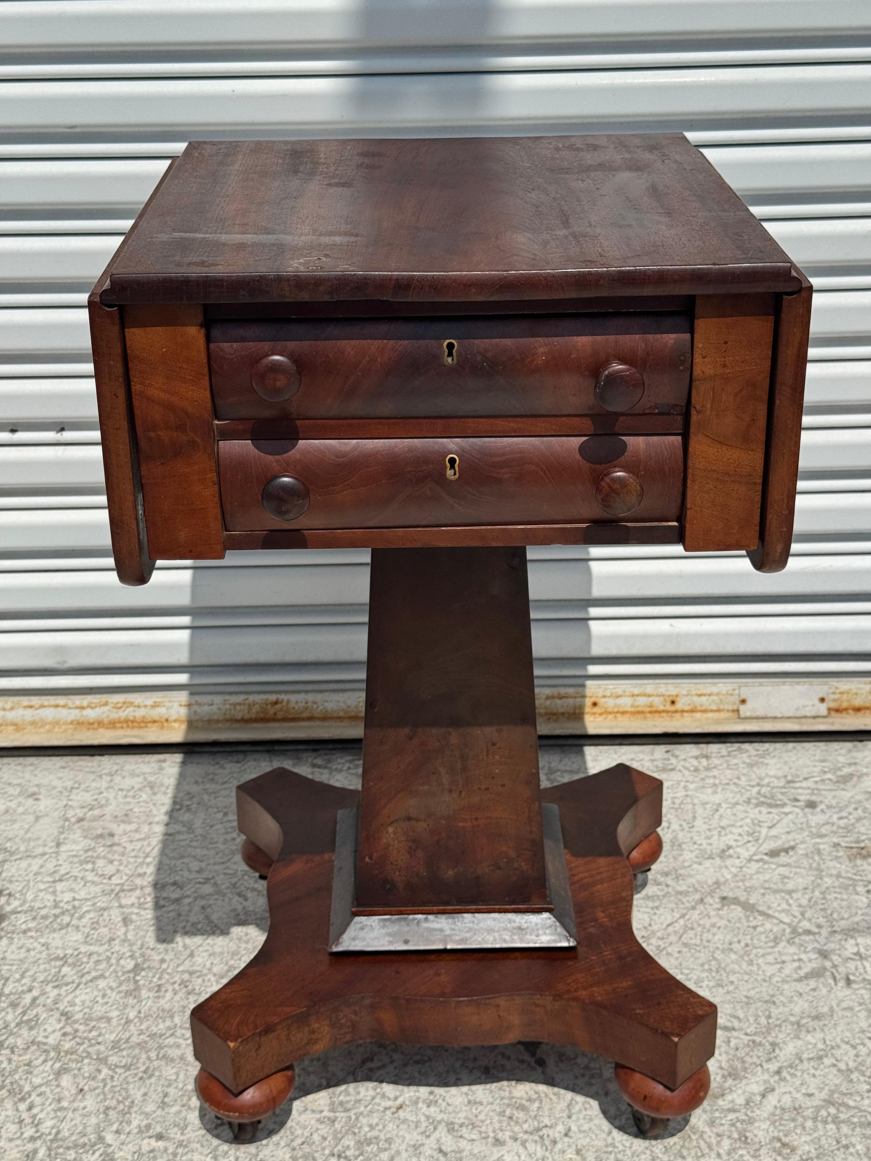 This is what they called a sewing or work table.
The table is made of flaming mahogany.
I has two drawers for storage and stands on a pedestal base.
The table has a pair of drop leaves that doubles the size of the top.
It sits on ball feet that rest