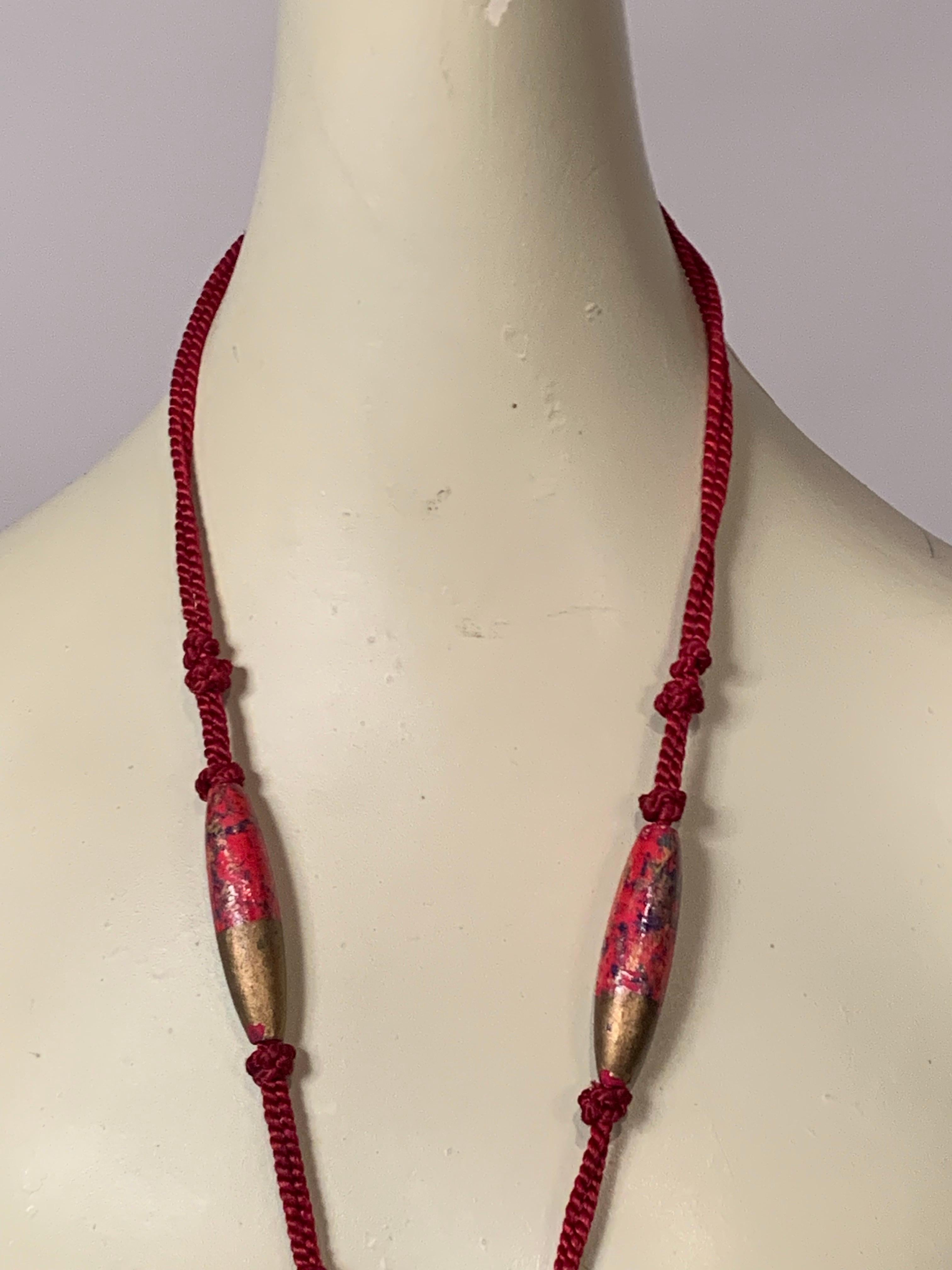 Encima se anuda un largo cordón de color rojo oscuro intenso 
y debajo cuatro largas cuentas de madera pintadas de colores. La estrella de este collar es el colgante de chica Flapper de los años 20 suspendido del collar de cordón. Tiene una cara