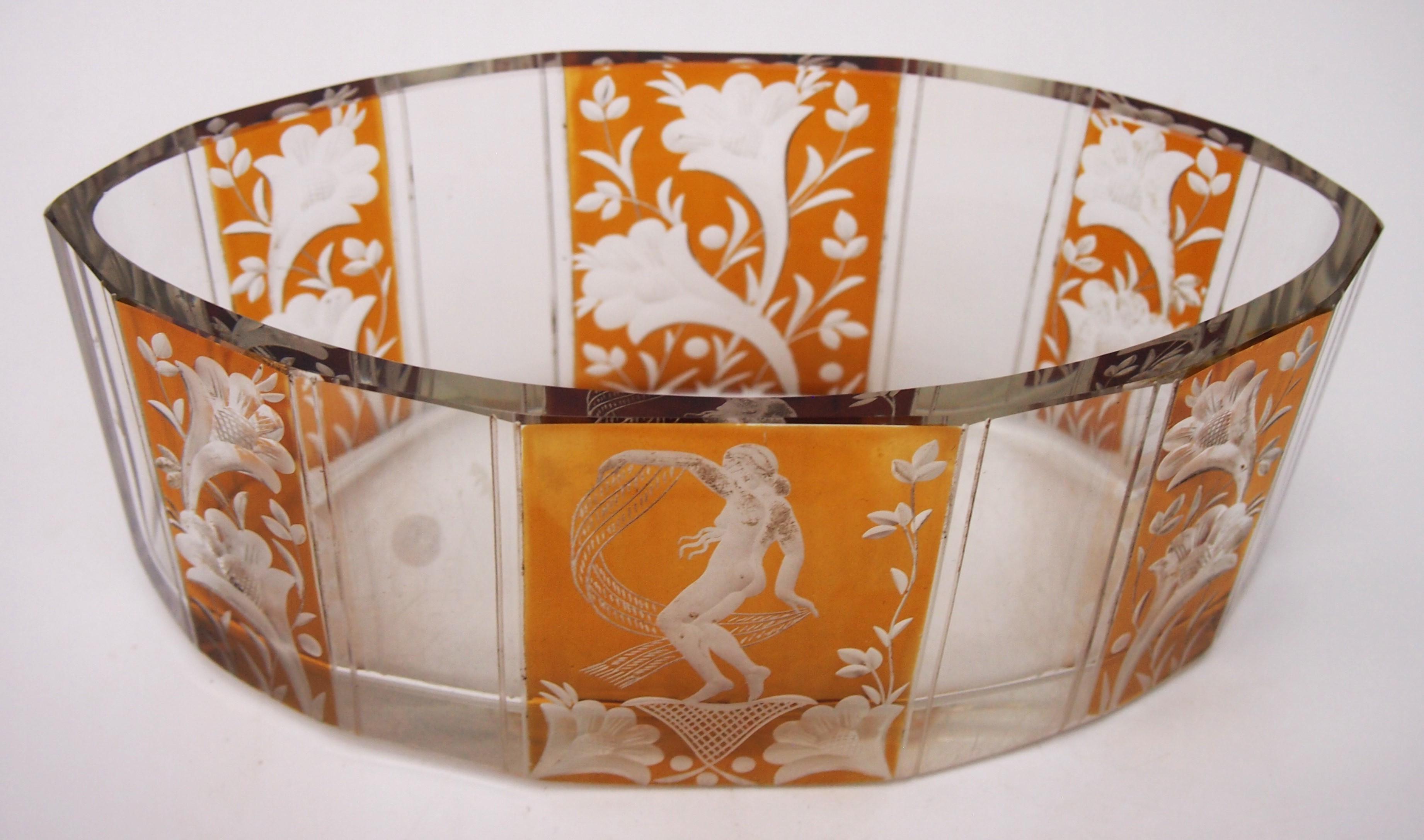 Un fabuloso Ámbar Haida de Fachschule, destellado sobre transparente, cuenco bajo tallado que representa en paneles alternados de ámbar y transparente uno con una bailarina exótica con velo y los otros con guirnaldas de flores. Produce una imagen