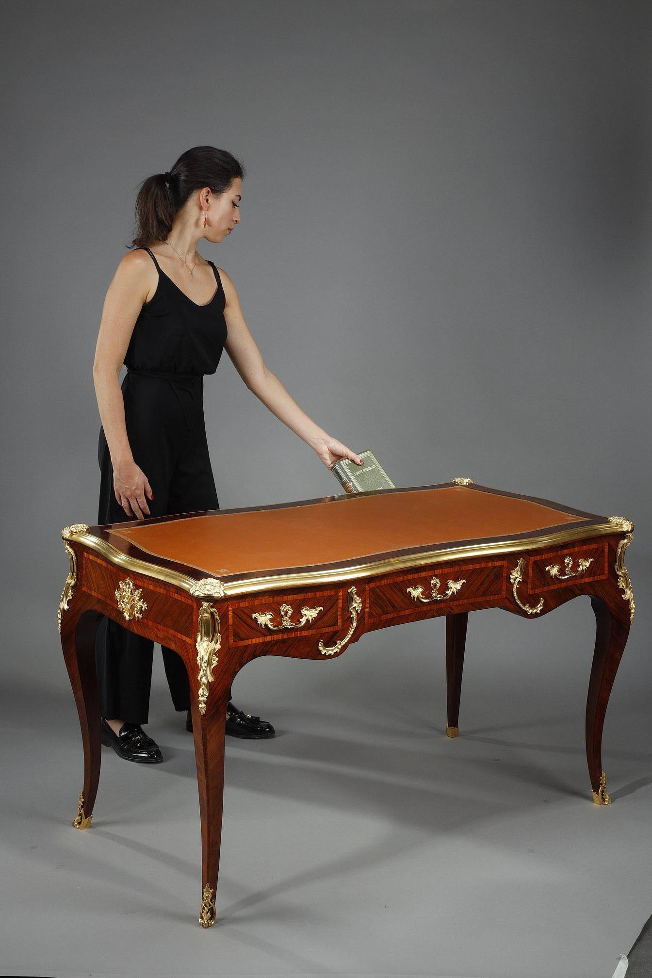 Important Louis XV style desk stamped Maurice RINCK, veneered with wood, richly decorated and marquetry, topped by a rectangular tray and covered with ocher leather. The leather girdled with a frieze of foliage and lilies gilded with iron, is