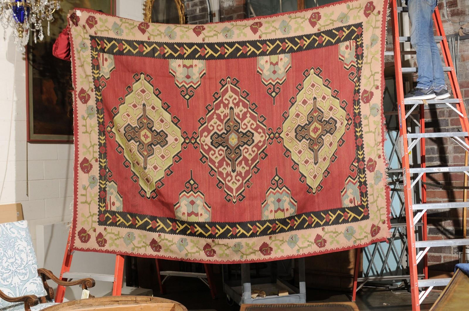 Kilim rug handwoven in the style of Karabakh featuring cream and red border with blue and red flowers and green vine work, black inner border with yellow and red floral motif and red inner area featuring geometric forms with blue green, red, black