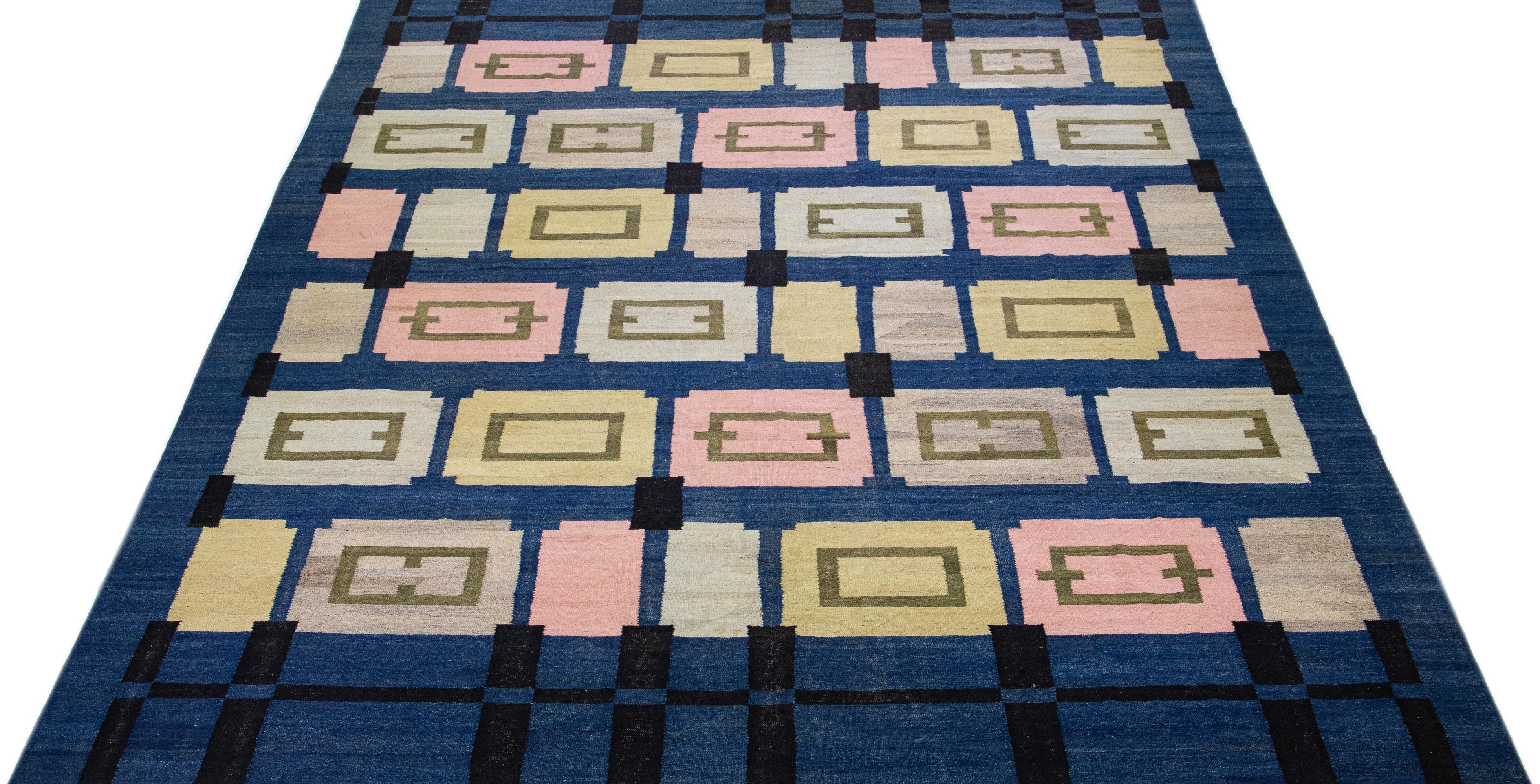 Beautiful Contemporary Kilim flatweave wool rug with a navy blue color field. This Oversize rug features a gorgeous geometric deco design in beige, pink, black, and green. This luxurious rug captures intricate details and a unique multi-dimensional