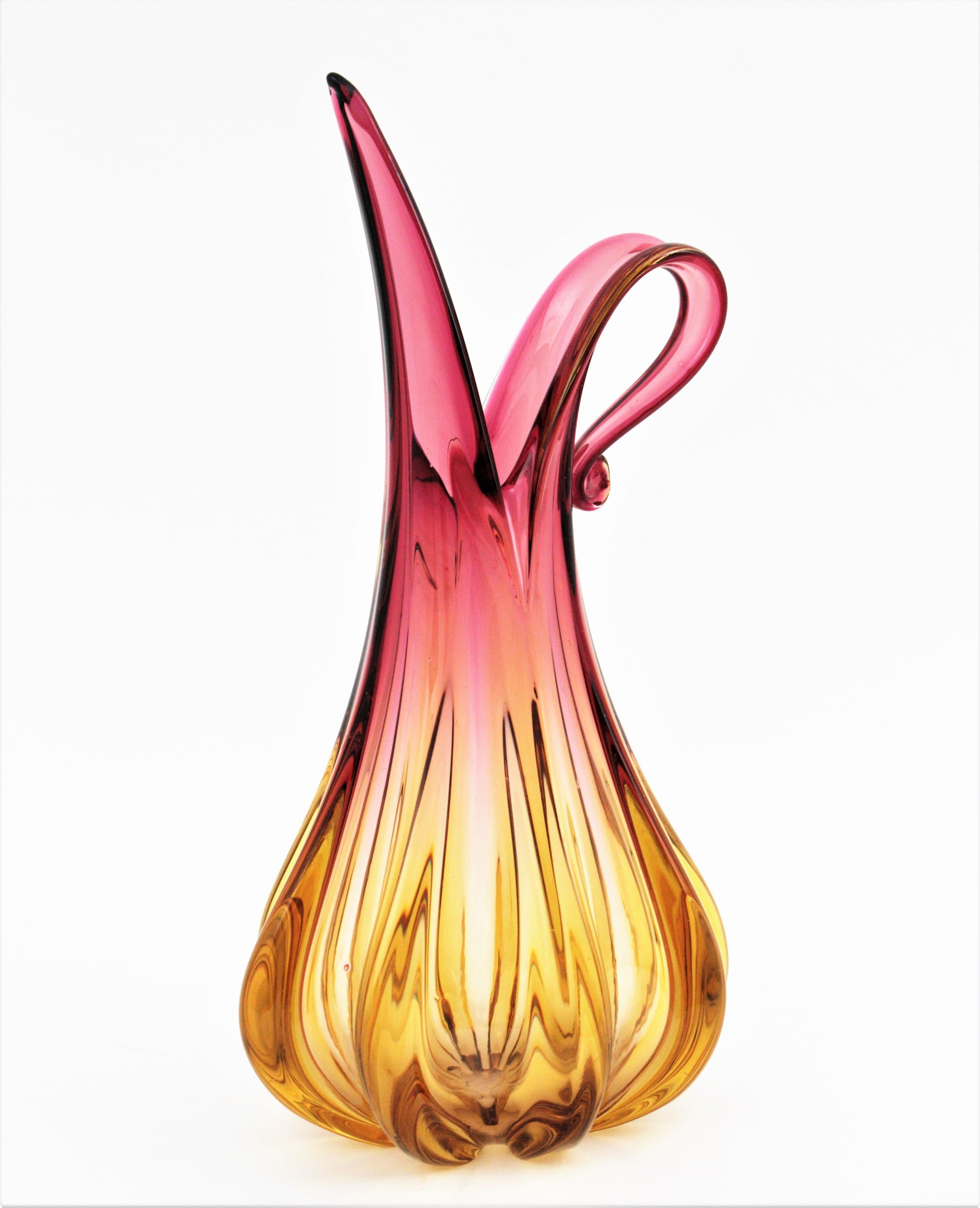 Skulpturale Murano Vase in Form eines Kruges aus rosa und bernsteinfarbenem Glas. Entworfen von Flavio Poli und hergestellt von Seguso Vetri d'Arte. Italien, 1950er Jahre.
Großes Format.
Lebendige Farben in einem Farbverlauf von rosa bis