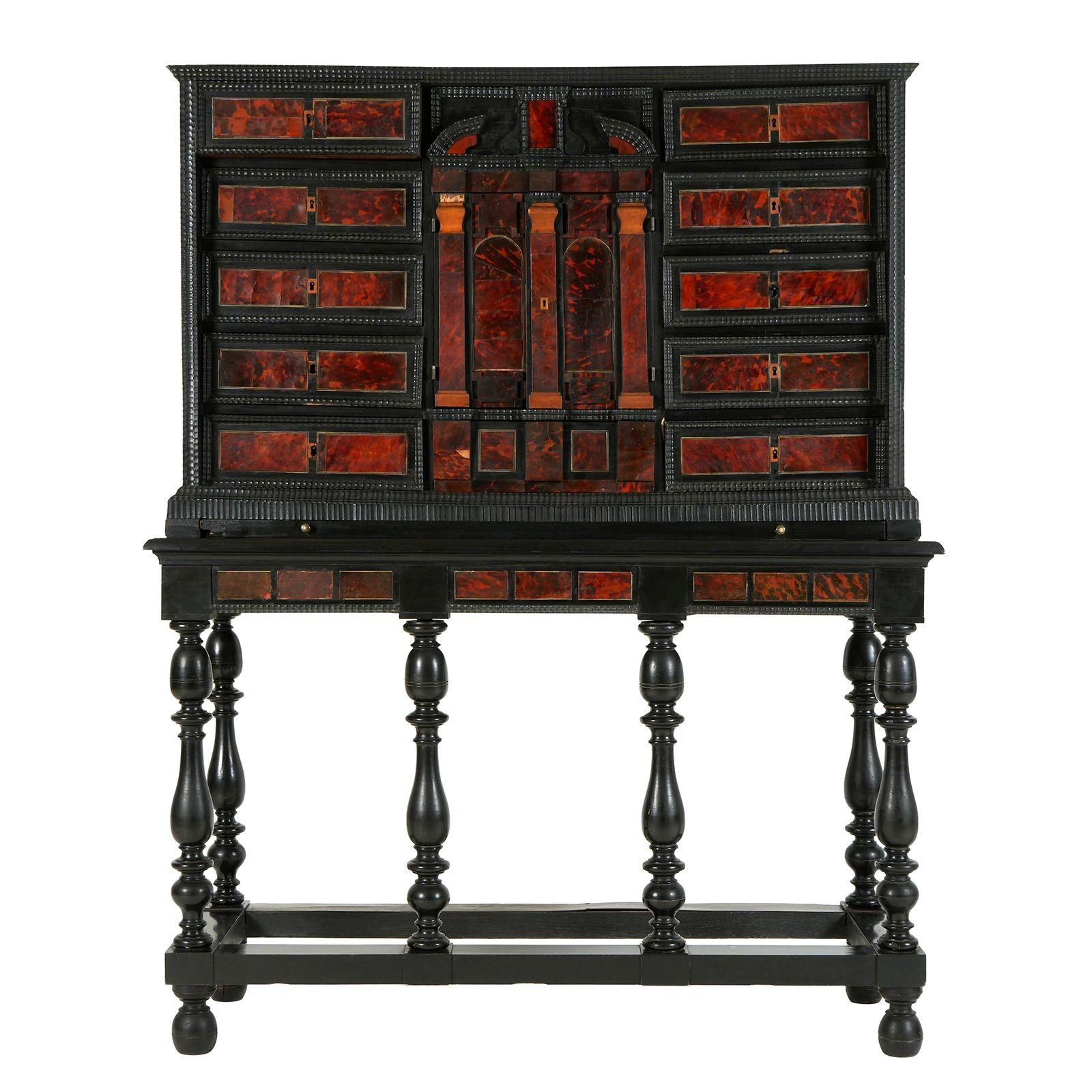 Un mueble tradicional flamenco de madera ebonizada, fabricado en Amberes en el siglo XVIII, con preciosas incrustaciones de carey, apoyado sobre un soporte con paneles de carey a juego y patas de bollo. Consta de dos puertas centrales flanqueadas