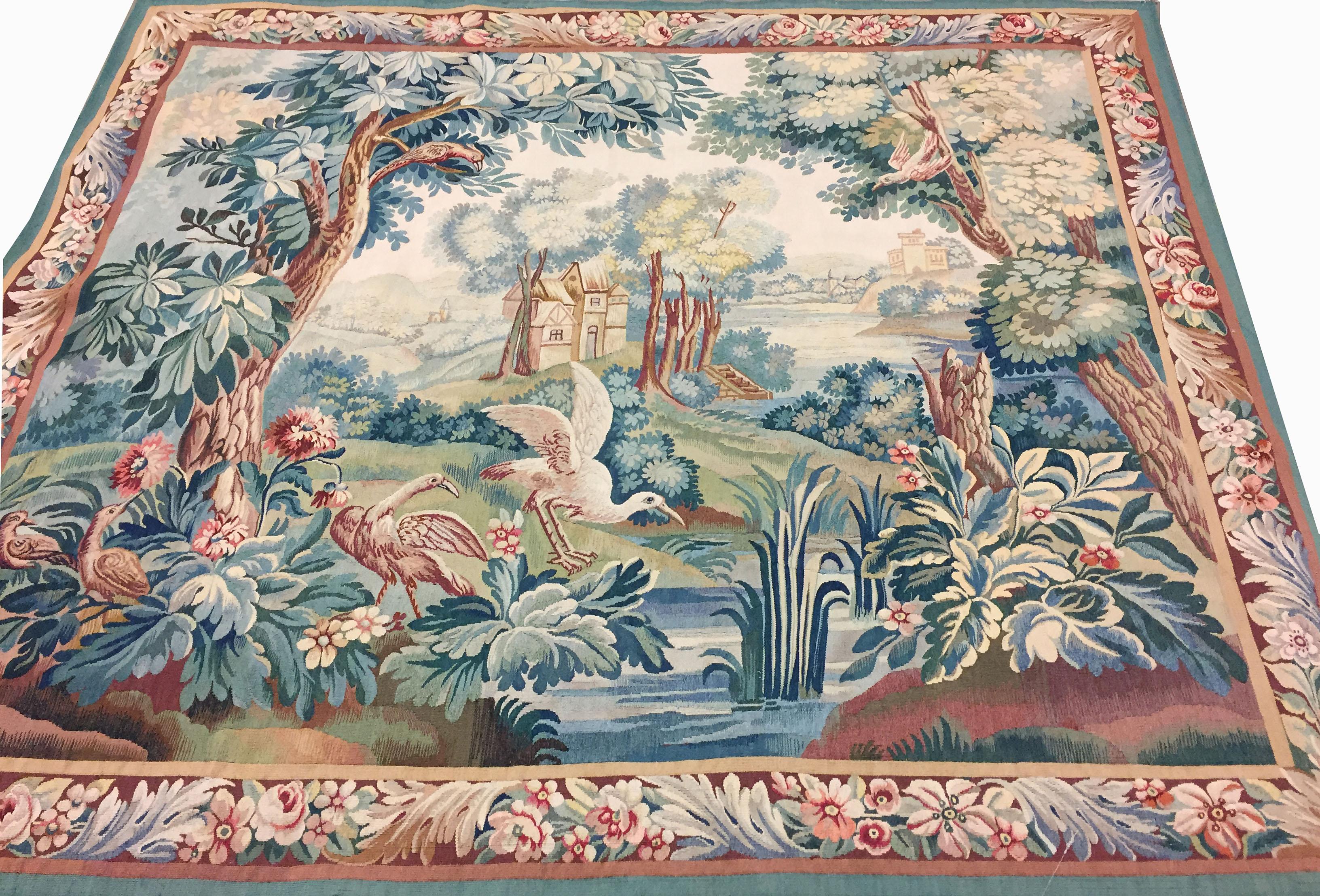 Flemish 19th century tapestry, a picturesque country scene with a stream winding its way through and two houses depicted. The swans enjoying themselves standing on the leaves with two birds perched on the trees. All surrounded by a colorful border