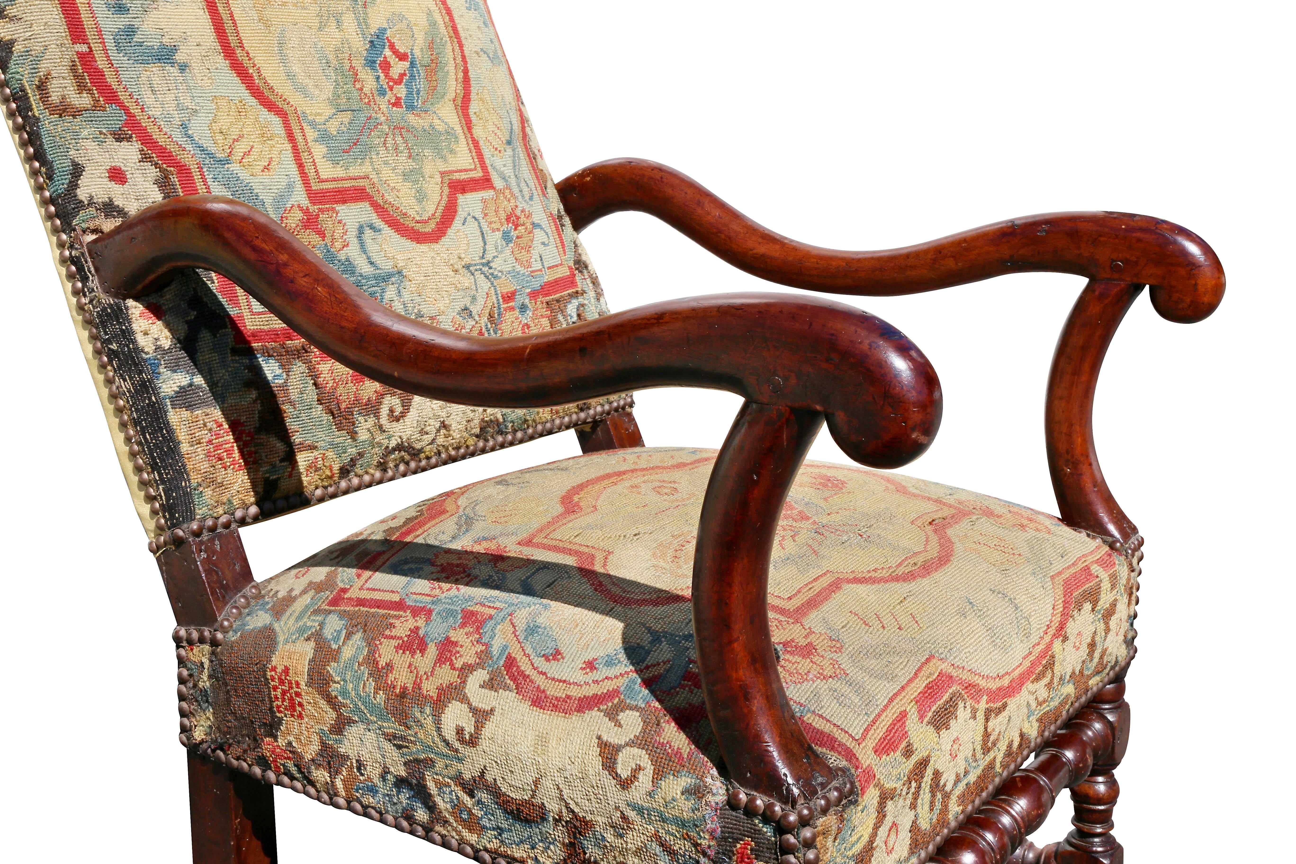 With arched needlepoint back and downswept curved arms, needlepoint seat raised on block and turned legs with conforming H form stretchers.