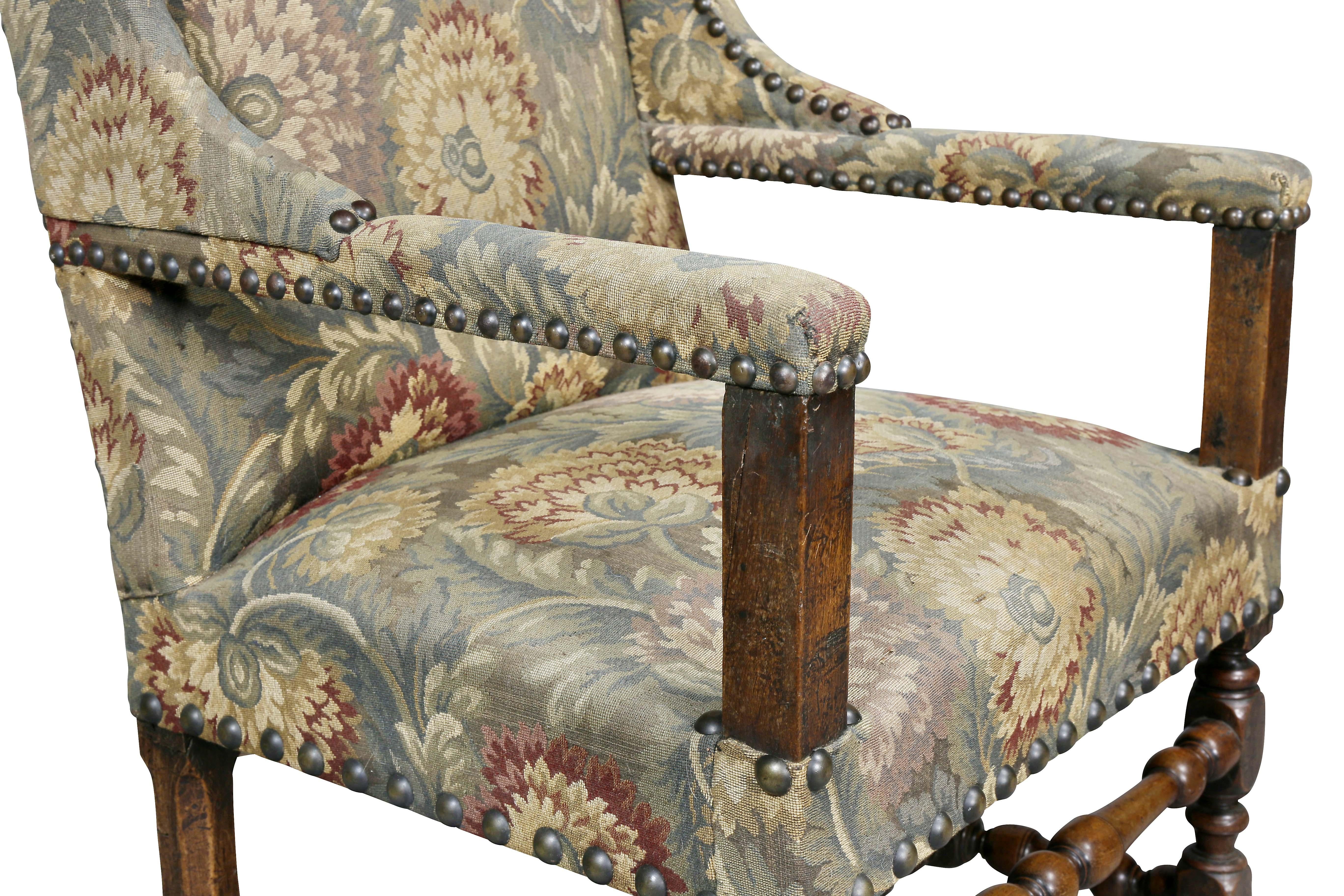 With upholstered wing back, straight arms and seat raised on turned legs with center and H form stretchers.