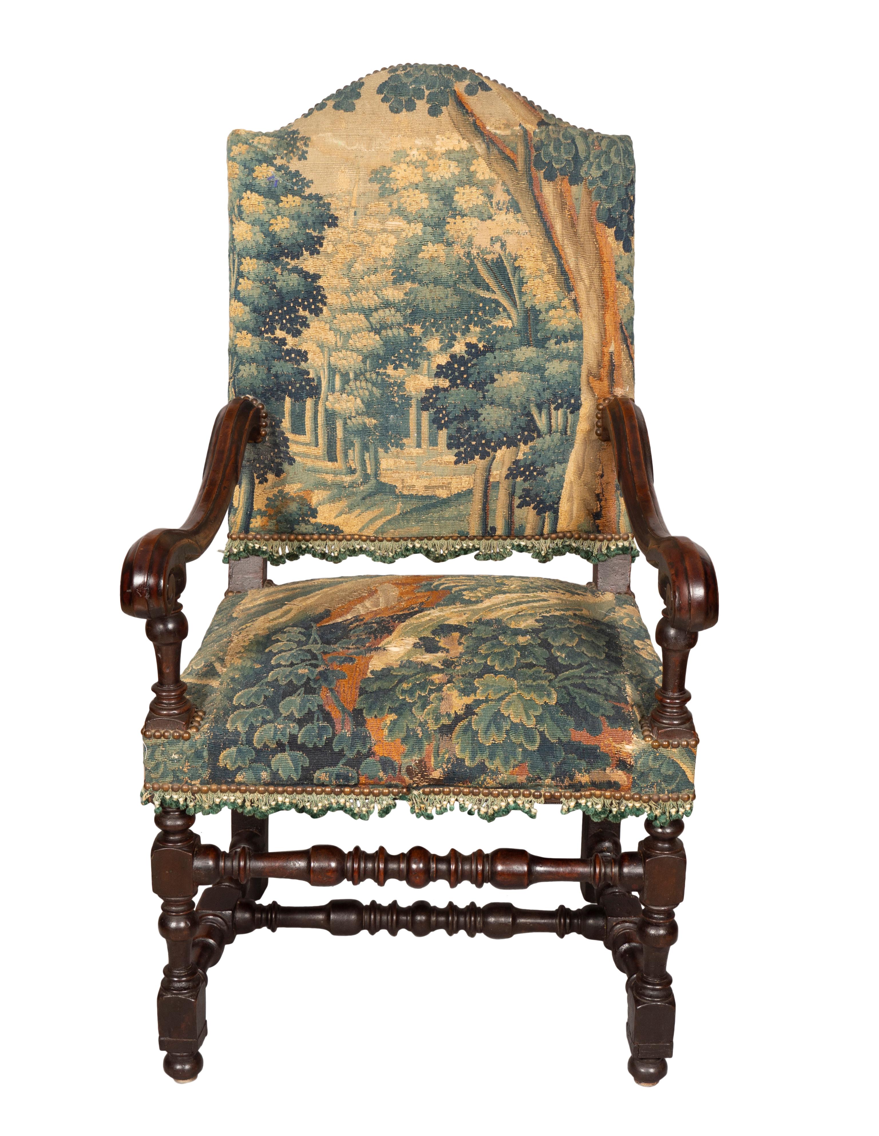 With an arched back and shaped carved arms , raised on turned legs and turned H form stretcher. Upholstered in period Flemish verdure tapestry as is.
