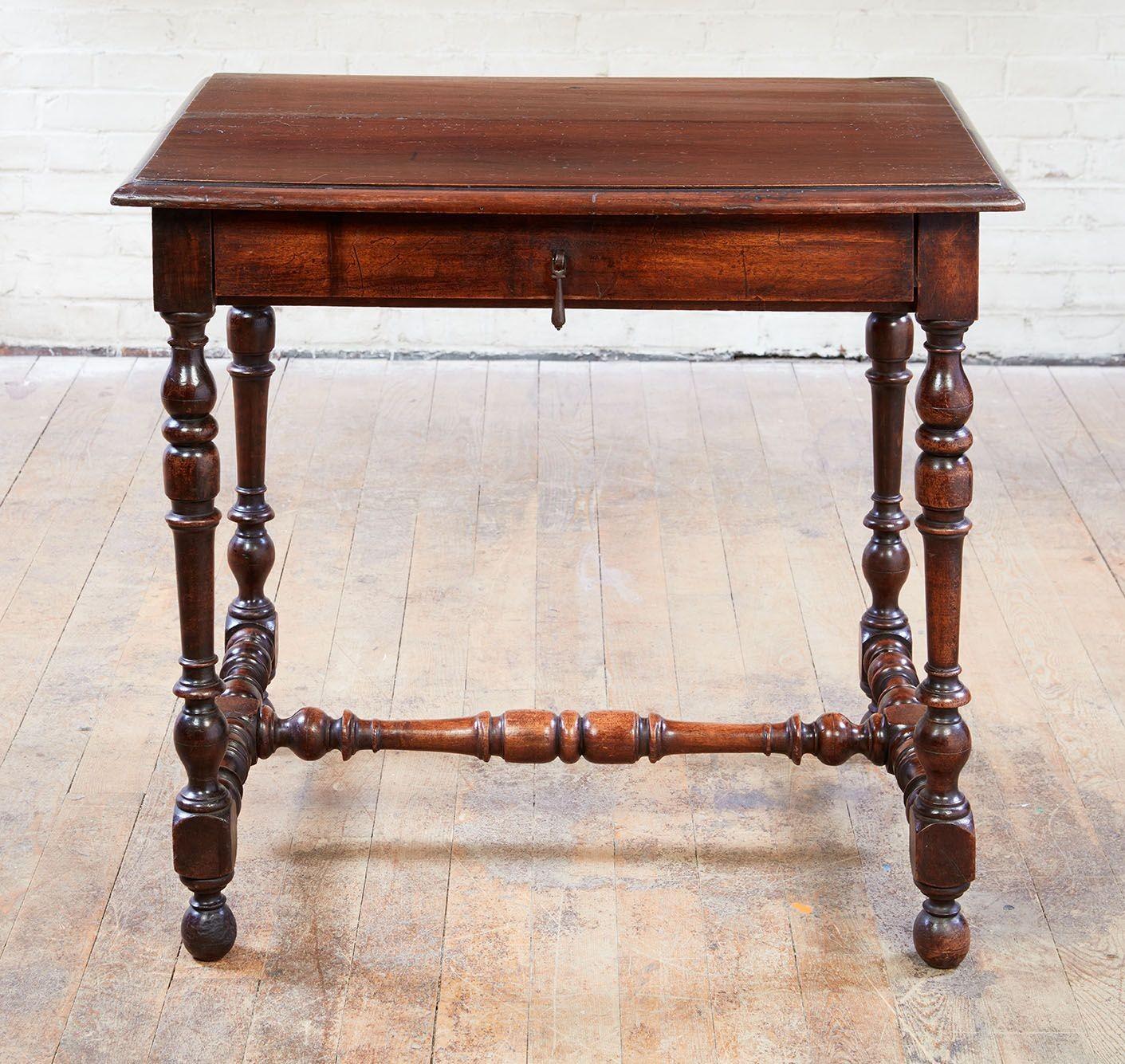 A Flemish Baroque side table in walnut with molded two plank top over single drawer with center drop pull and standing on turned legs joined by conforming turned H-shaped stretcher. Flemish or French 18th century.