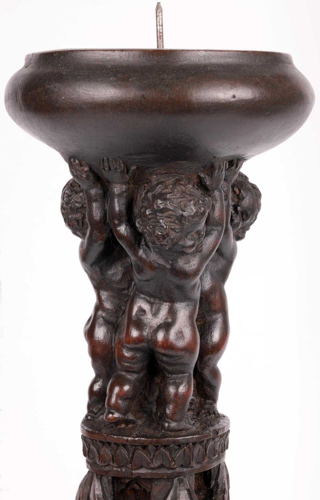 A beautifully carved antique Flemish wooden pricket candlestick with putti dating from the late 16th or early 17th century. The floor standing candlestick has a round bowl shaped top with the central spike candle holder, the top supported by three