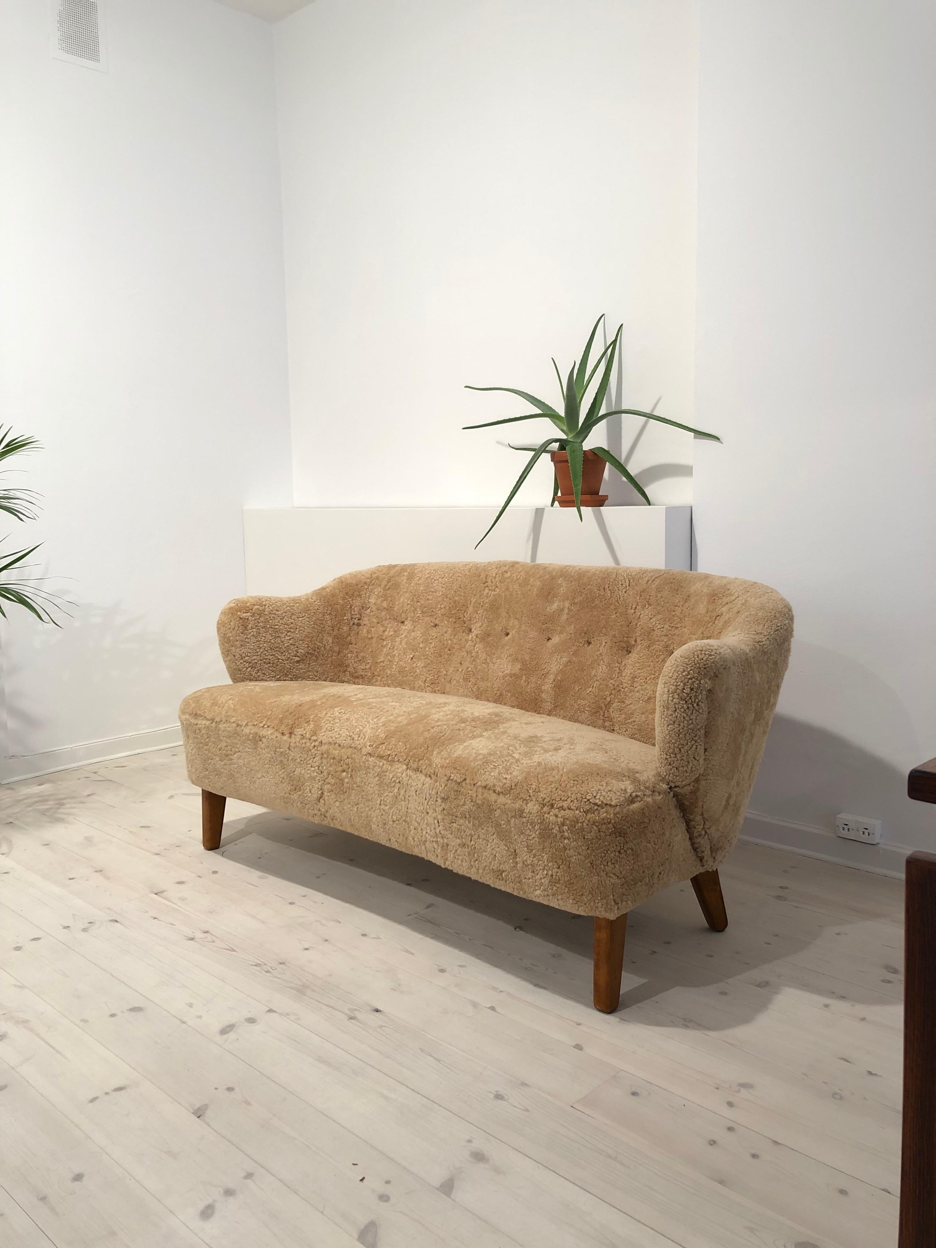 Flemming Lassen, two-seat settee for master cabinetmaker Jacob Kjær, Copenhagen. Natural/honey colored sheepskin upholstery, leather buttons and stained ash legs. Designed 1940.

Please view 1stdibs item reference number LU1081213317962 for pair