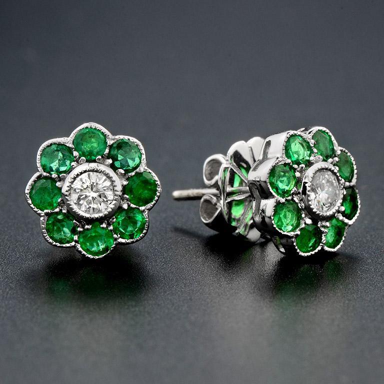 Dainty, sparkly, and glowing with a peppy green color. These diamond studs are crafted in 18K white gold and trimmed in emeralds. Each earring features a round diamond, surrounded by a cluster of emeralds. The emeralds have been set to resemble